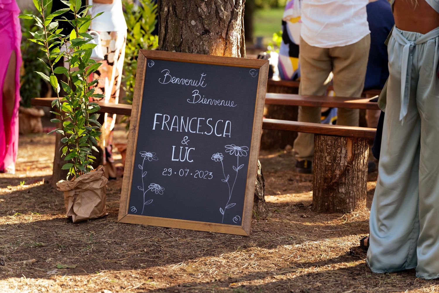 Rustic chalkboard sign displaying 'Francesco' and a date placed among trees at an outdoor wedding.