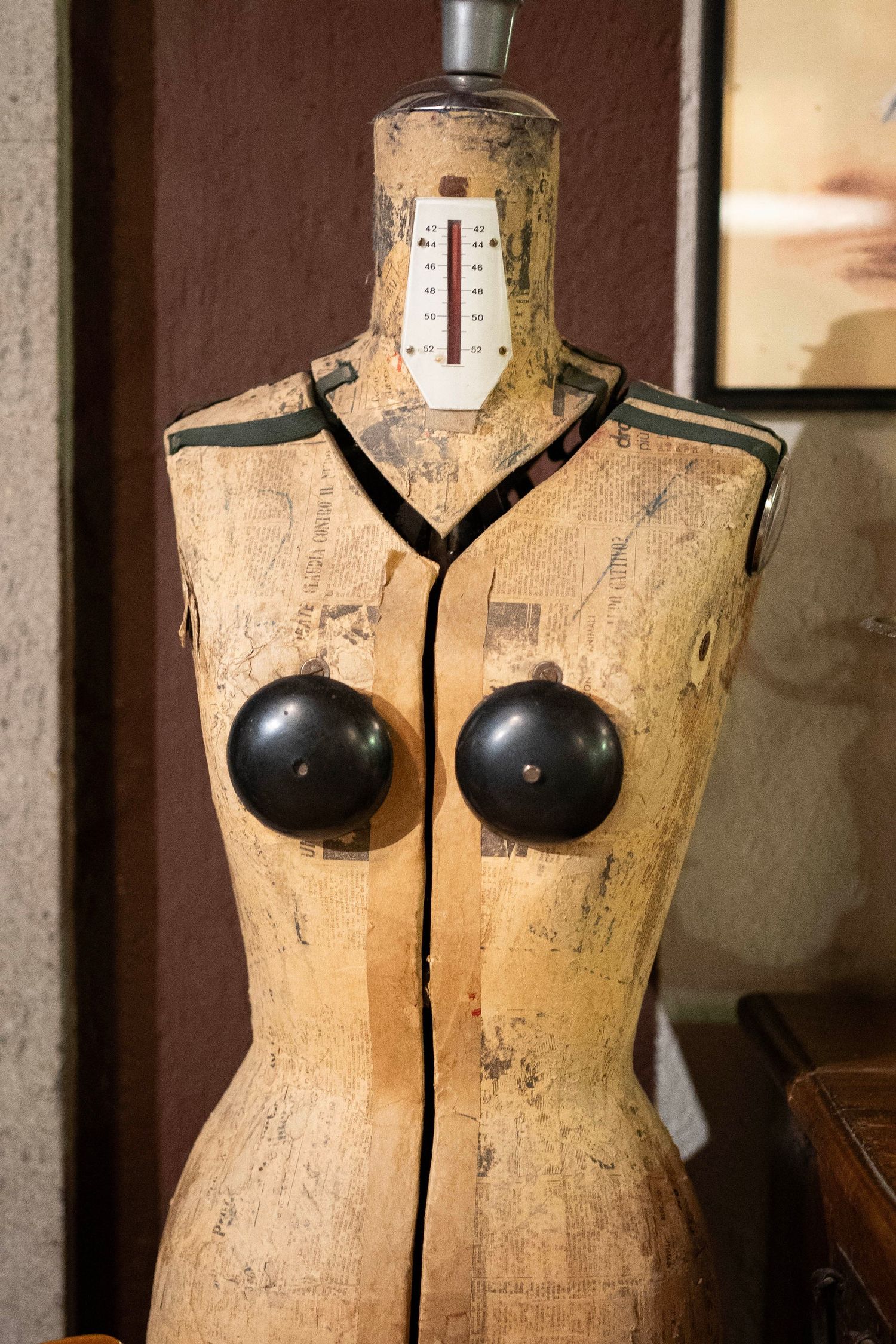 Vintage dressmaker form with temperature gauge and black decorative elements against brown wall.