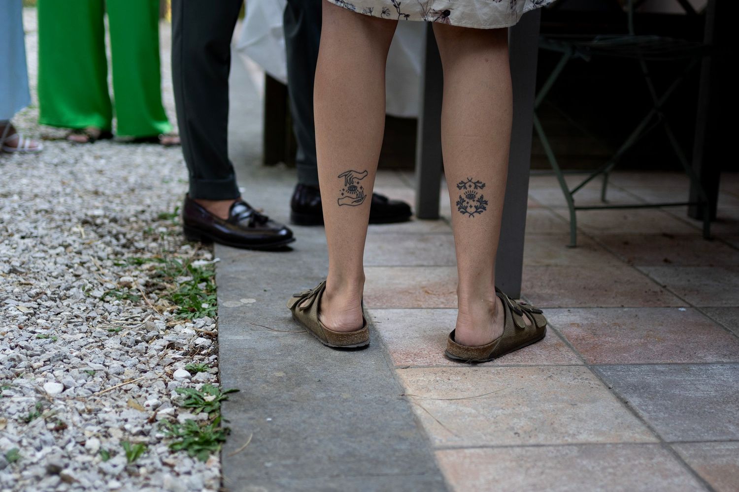 Legs with flowered tattoos visible below a dress hem on stone flooring.