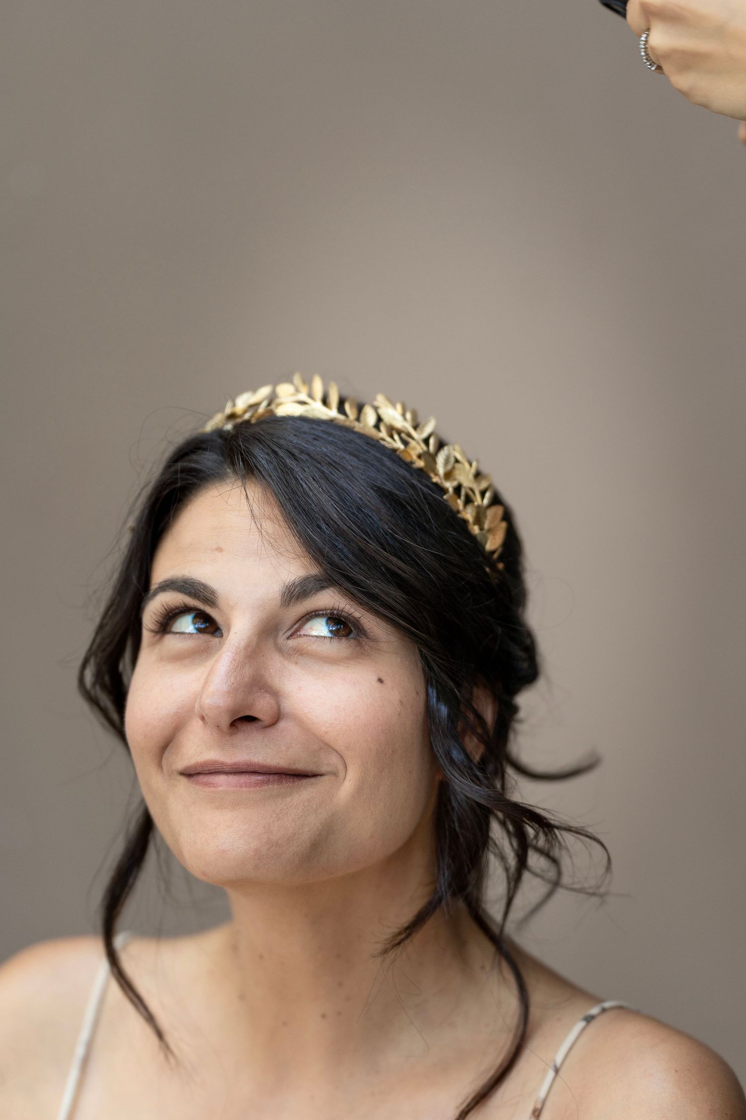 A person in a gold crown and beige straps glances upward with a gentle smile.