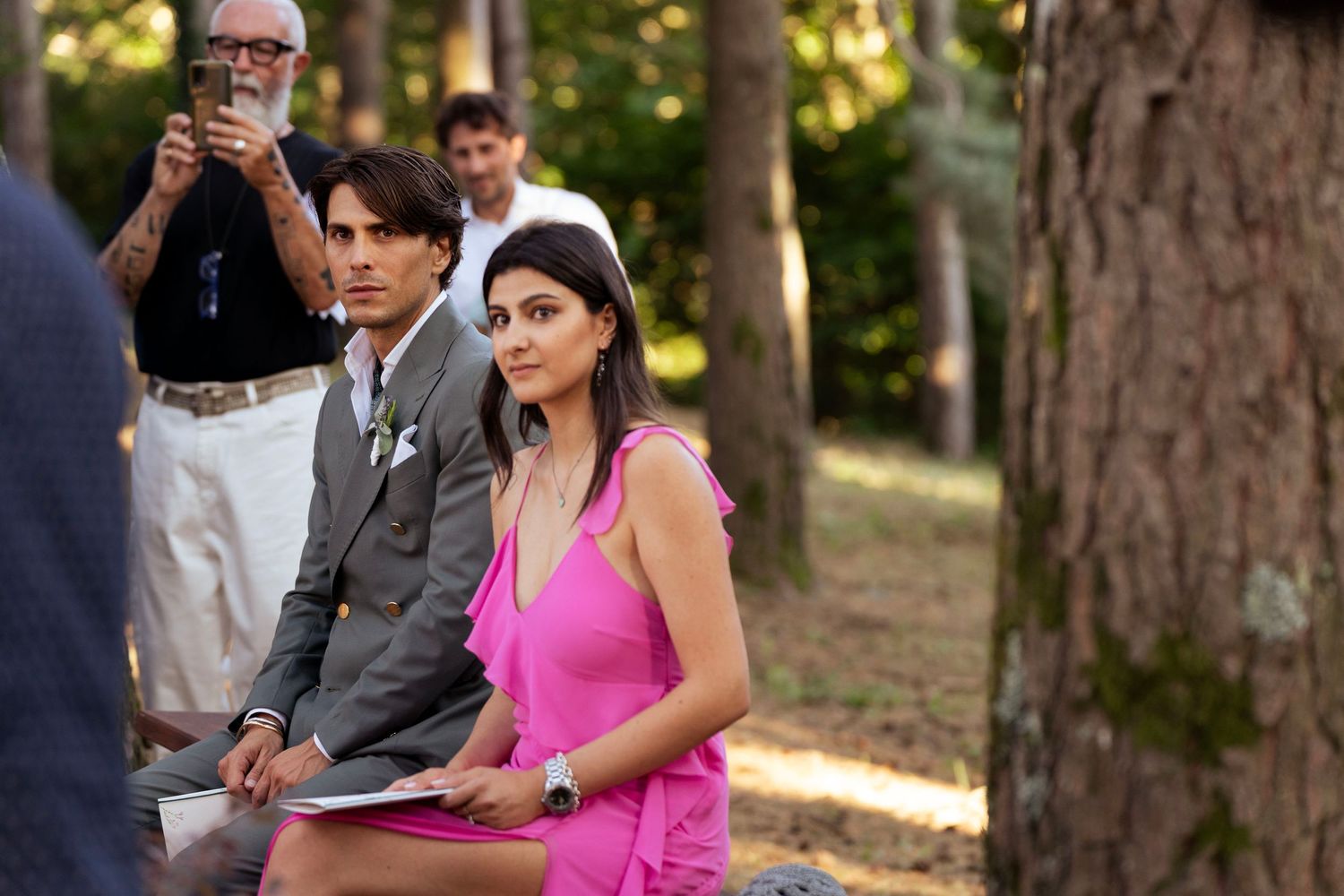 Wedding guests seated outdoors among pine trees during a forest ceremony.