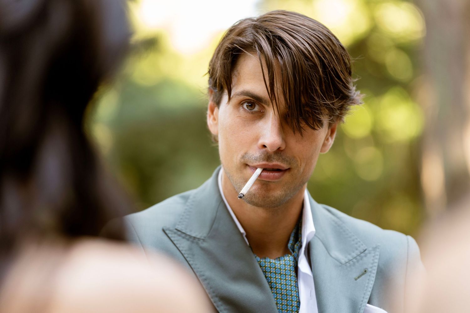 A person in a grey suit jacket and patterned tie looks intensely at the camera.