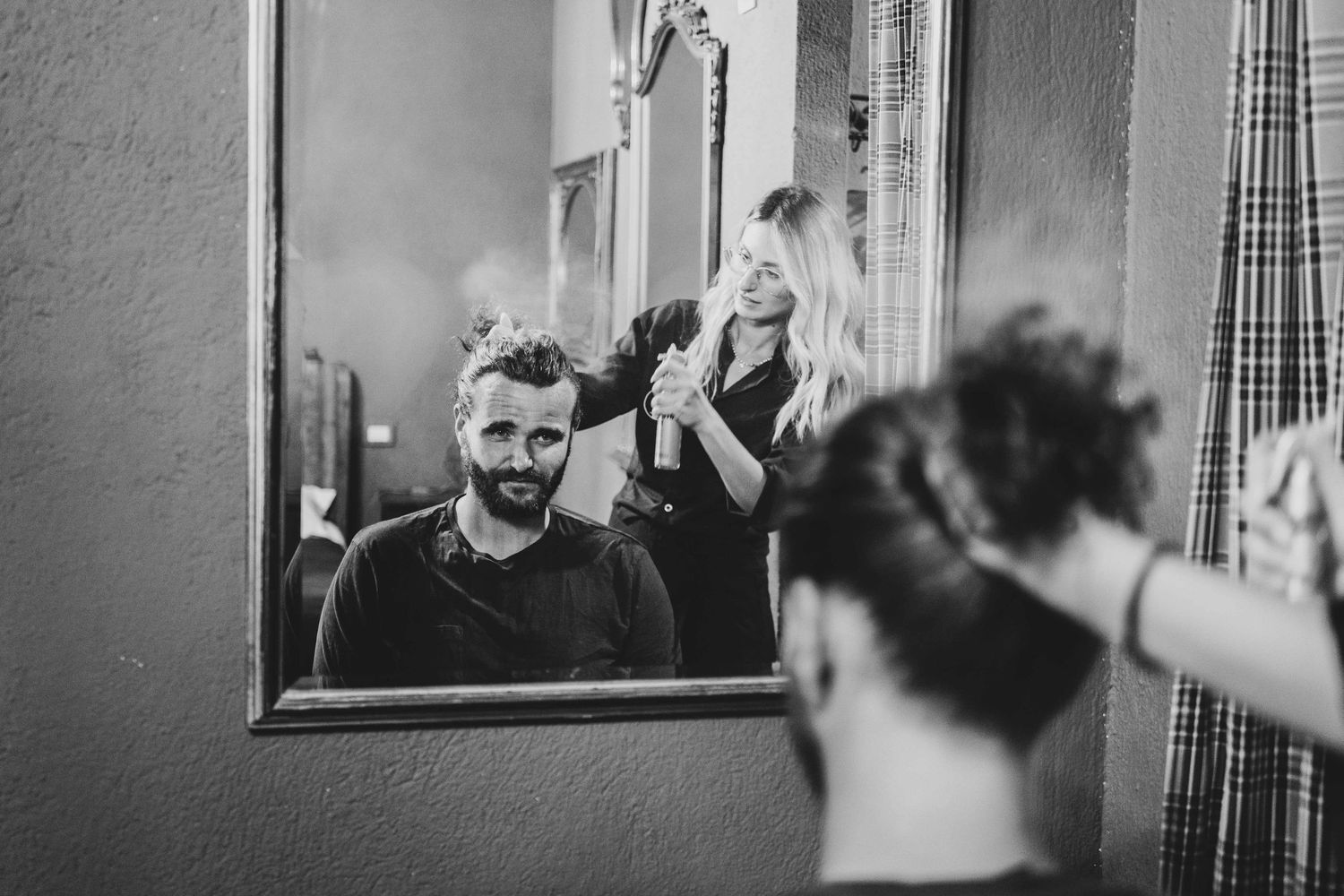 A black and white reflection in a mirror showing someone getting hair styled.