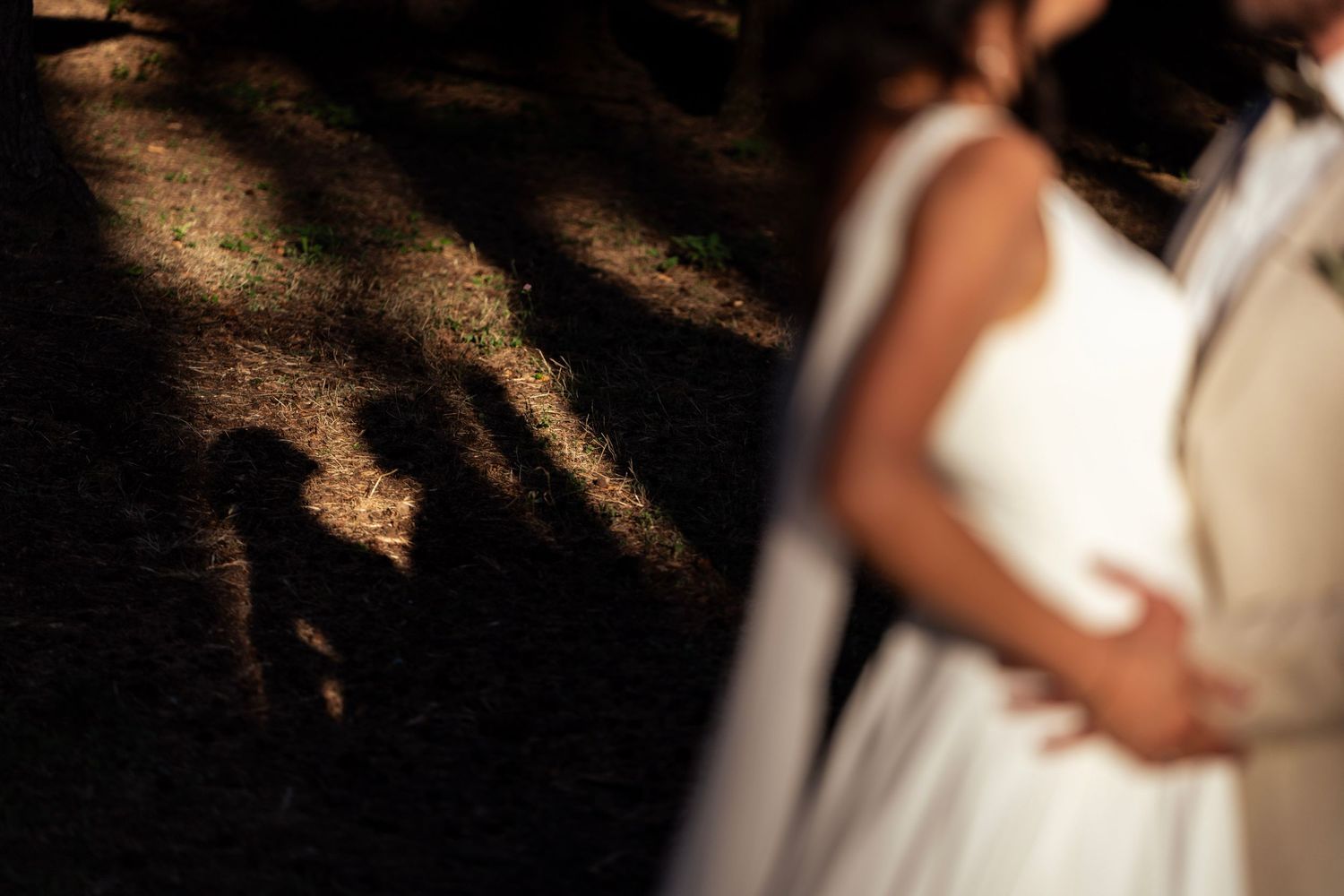 Artistic silhouette of a wedding couple embracing in dappled forest light.