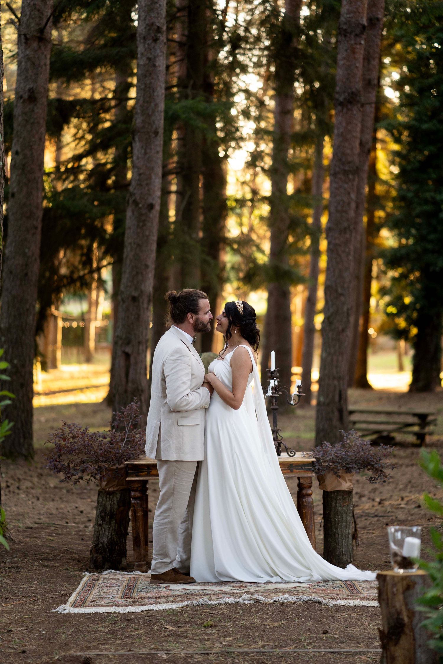 A romantic wedding portrait on a rustic rug in a forest setting with golden sunlight.