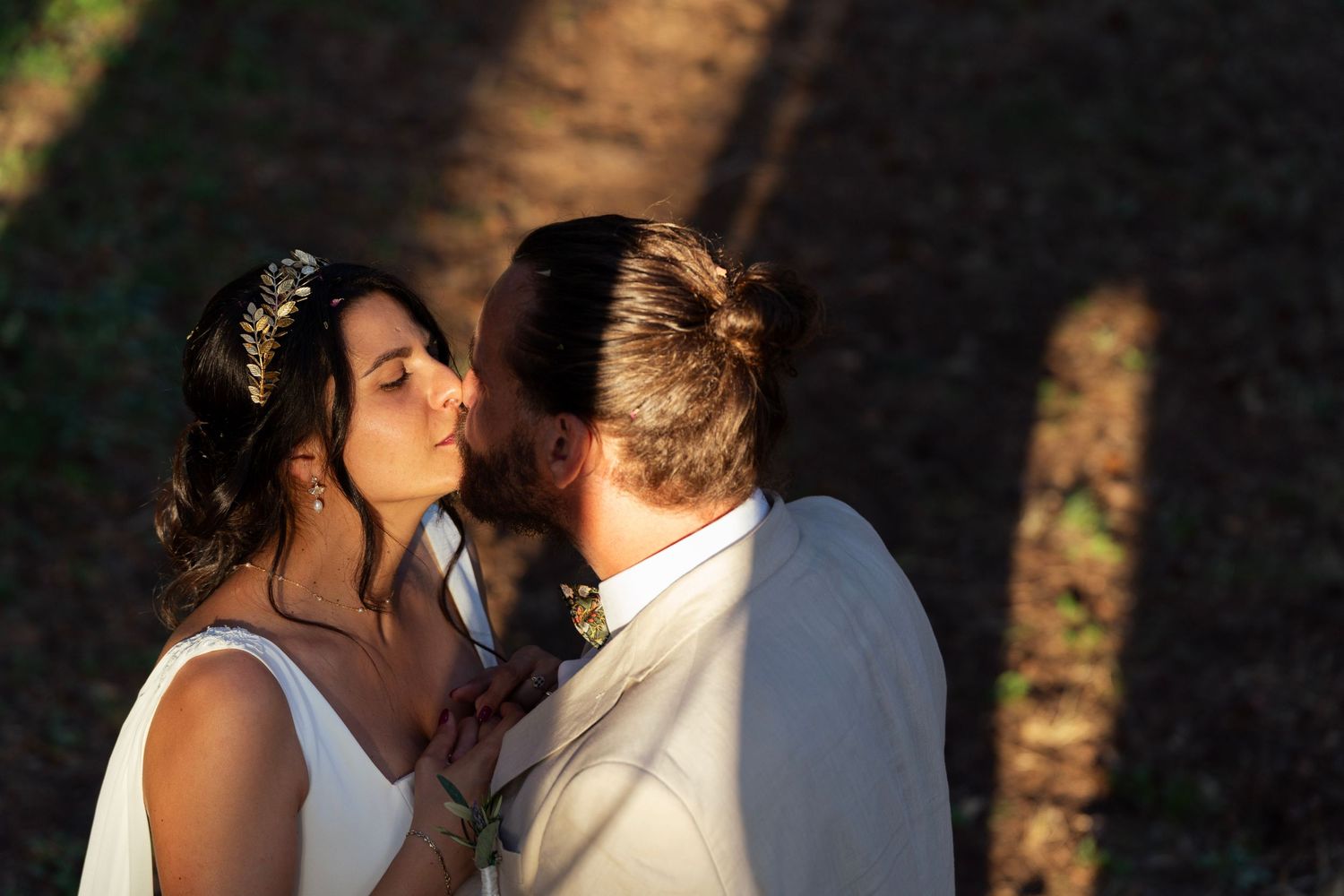 A romantic wedding moment captured in warm sunlight with shadows falling across a forest setting.