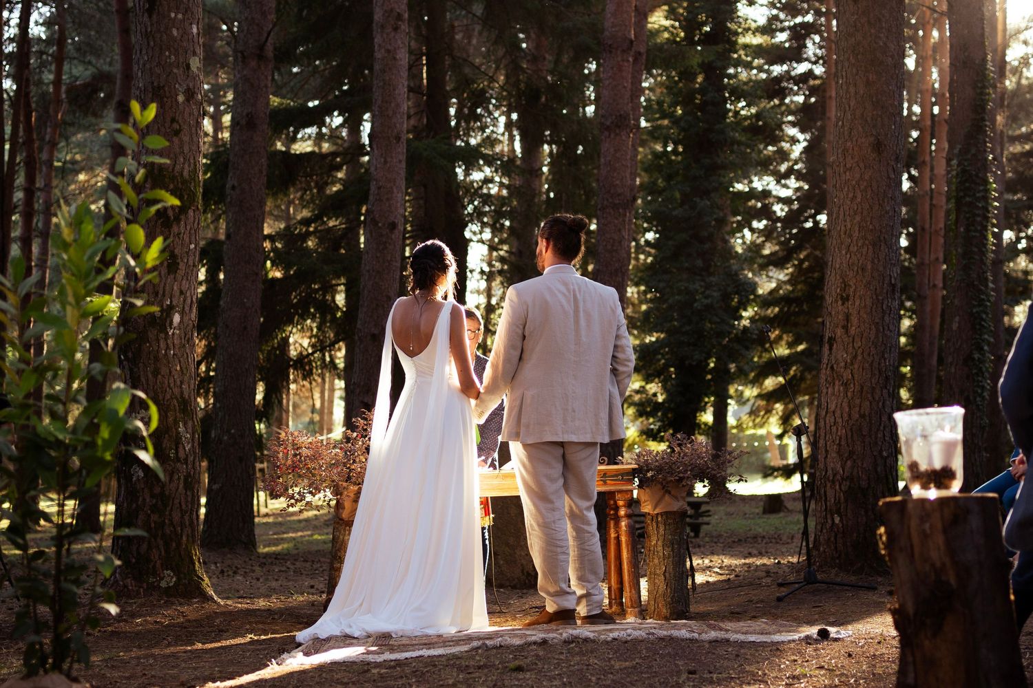 Newlyweds stand together in a sun-dappled forest setting.