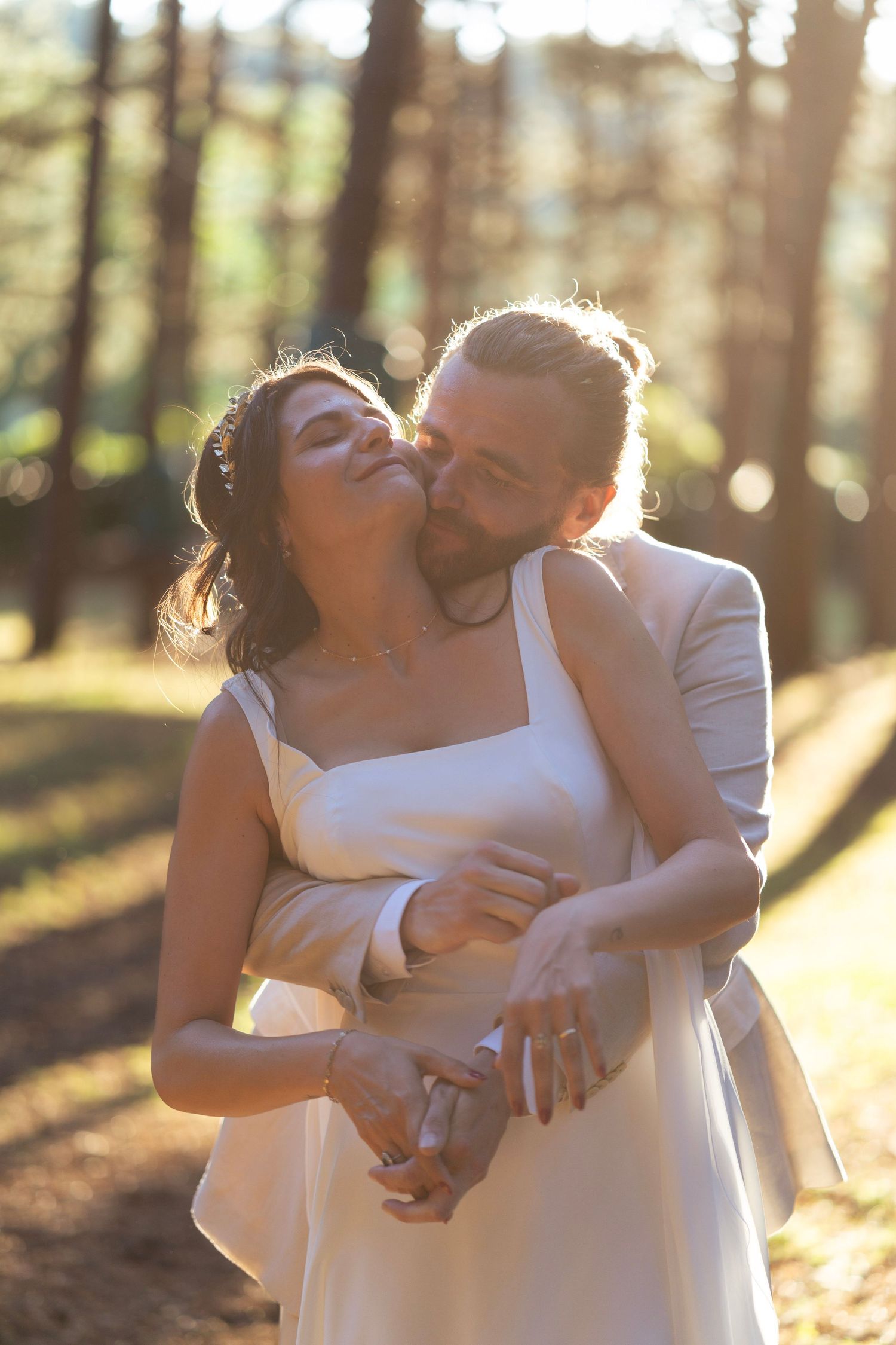 A joyful wedding embrace captured in golden forest light during sunset.