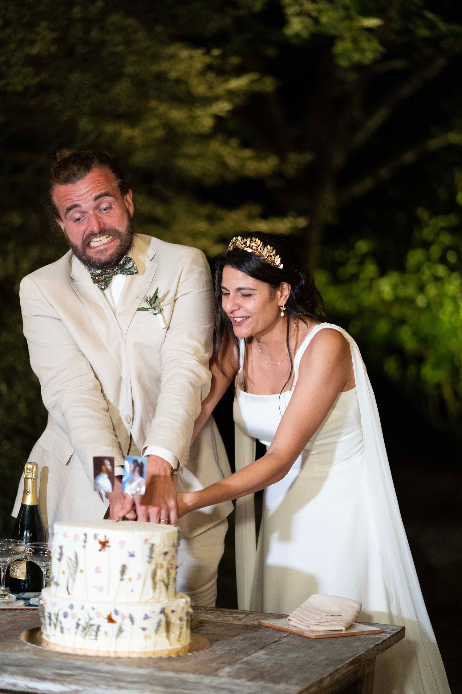 Newlyweds cut their wedding cake together while sharing a joyful moment outdoors.