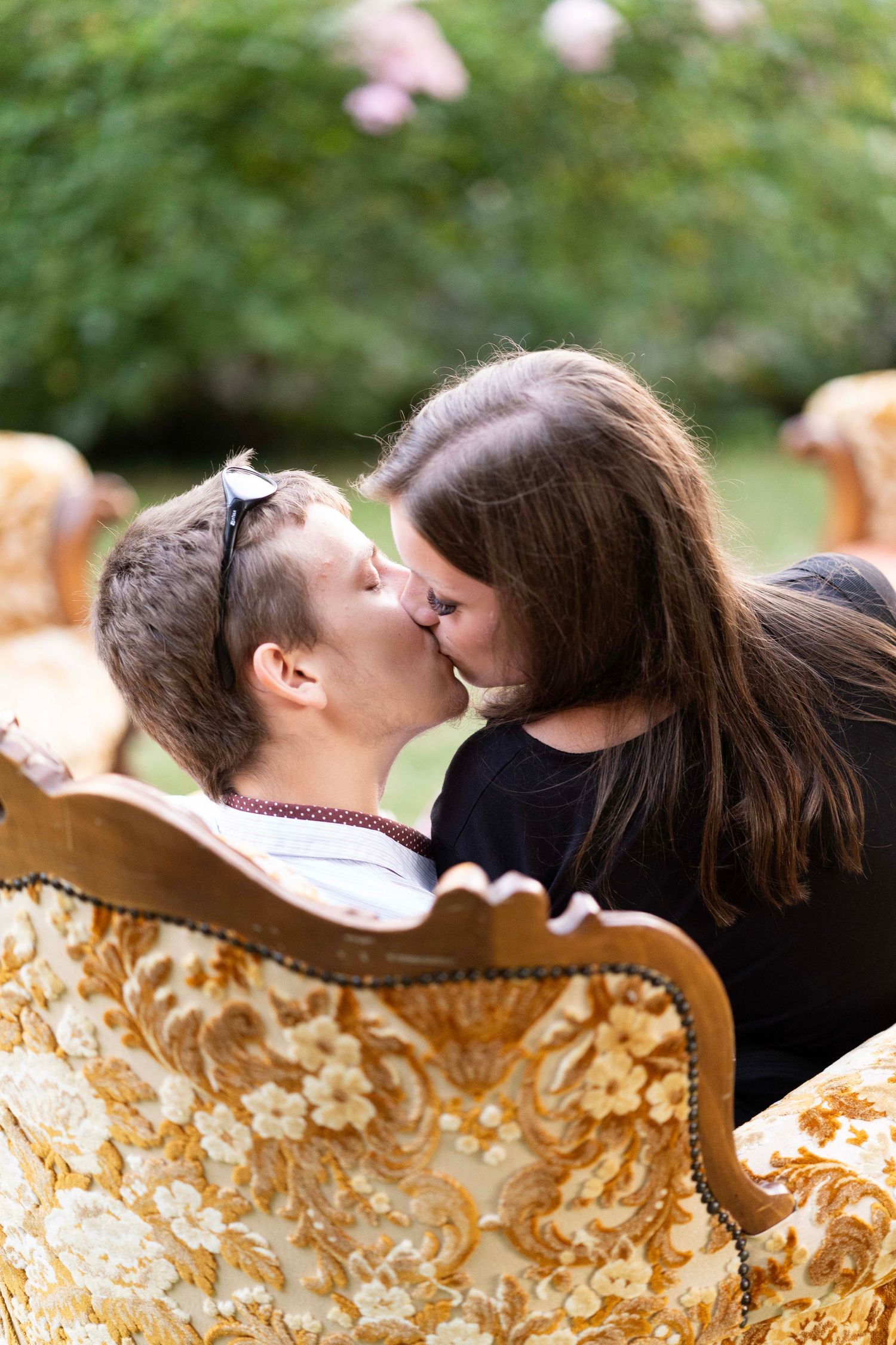 A tender moment shared on an ornate vintage floral sofa in a garden setting.