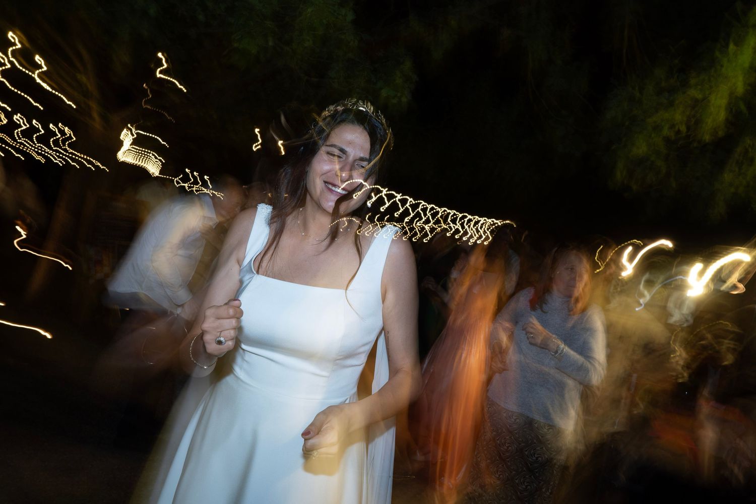 Dancer in white dress moves energetically under string lights at night celebration.