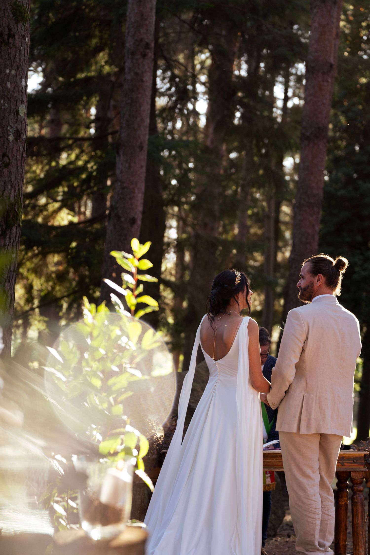 Couple stands together in a sun-dappled forest clearing during an intimate outdoor wedding ceremony.