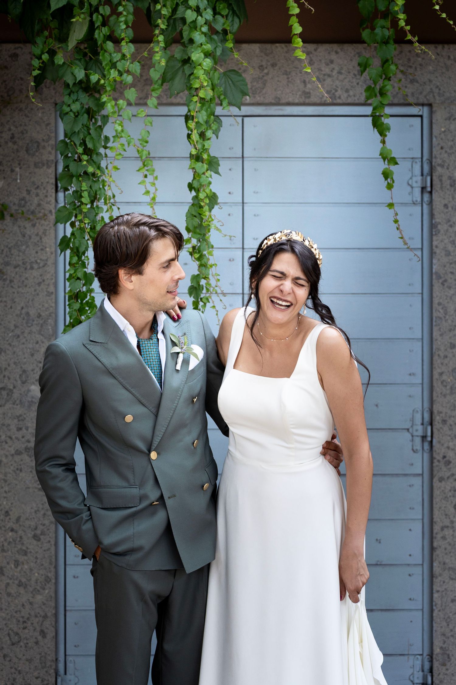 Joyful wedding moment captured against blue door with hanging green vines.