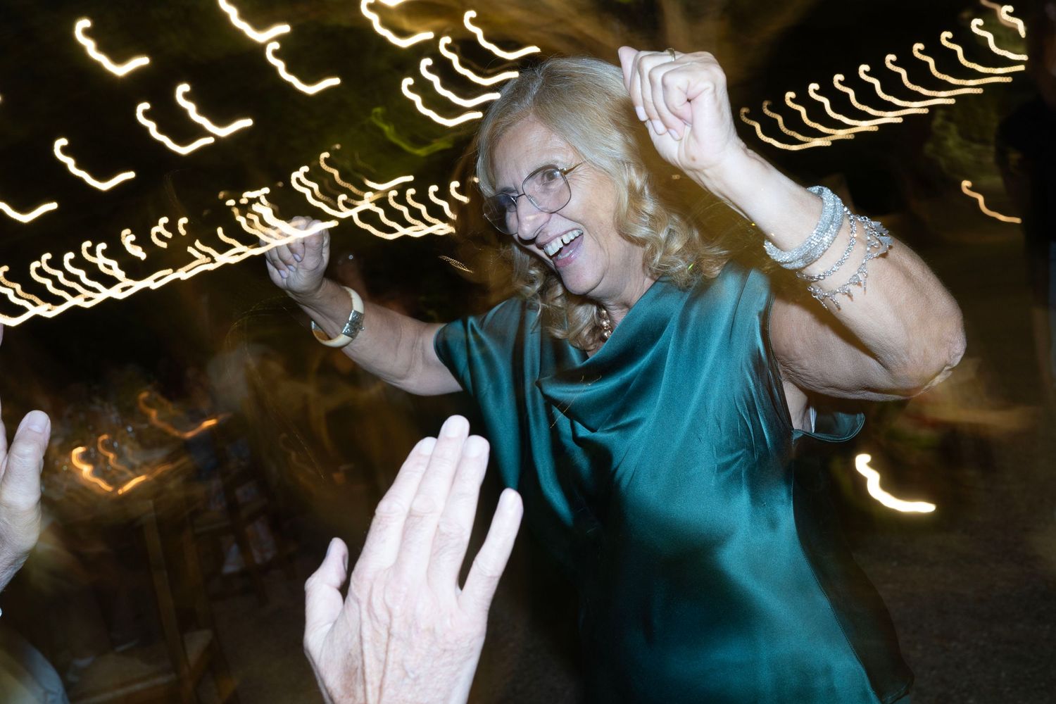 Party attendee dances joyfully under swirling light trails at night.