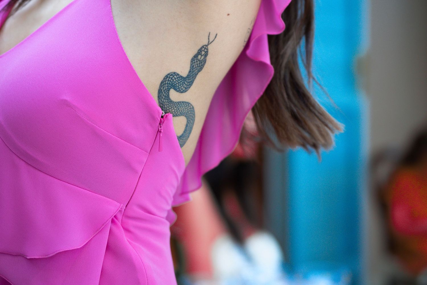 Small snake tattoo visible on shoulder through pink ruffled clothing.