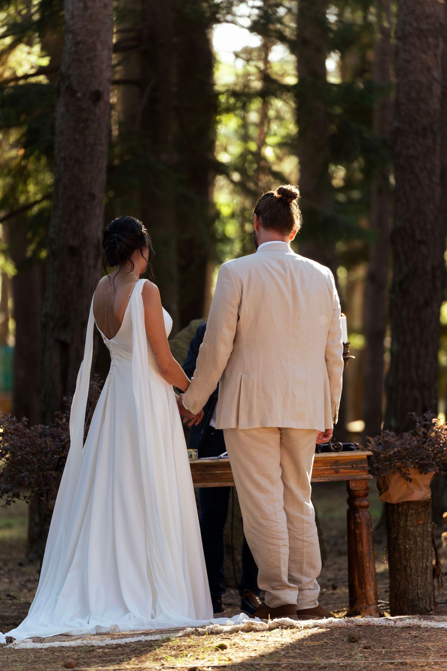 Couple in wedding attire standing at rustic wooden altar in forest setting.