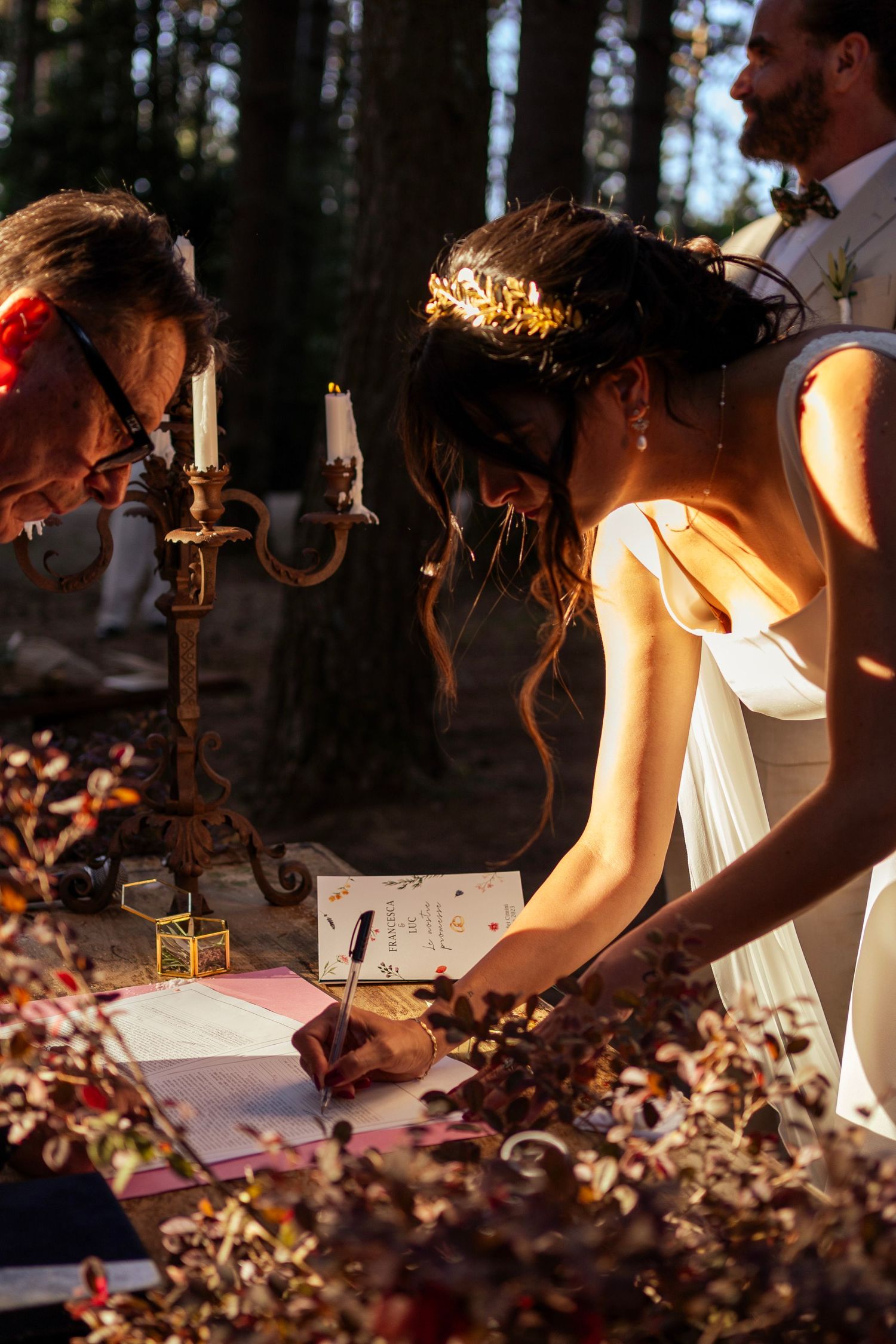 Signing of marriage documents by candlelight during an outdoor forest wedding.