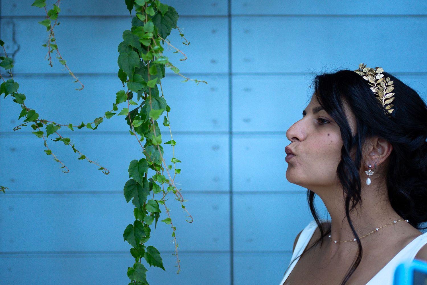 Elegant profile pose against blue wall with cascading green vines.