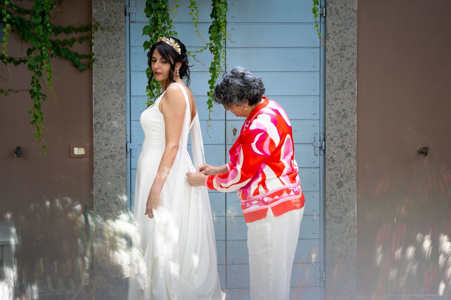 Wedding preparation scene with white dress against blue wall with hanging green vines.