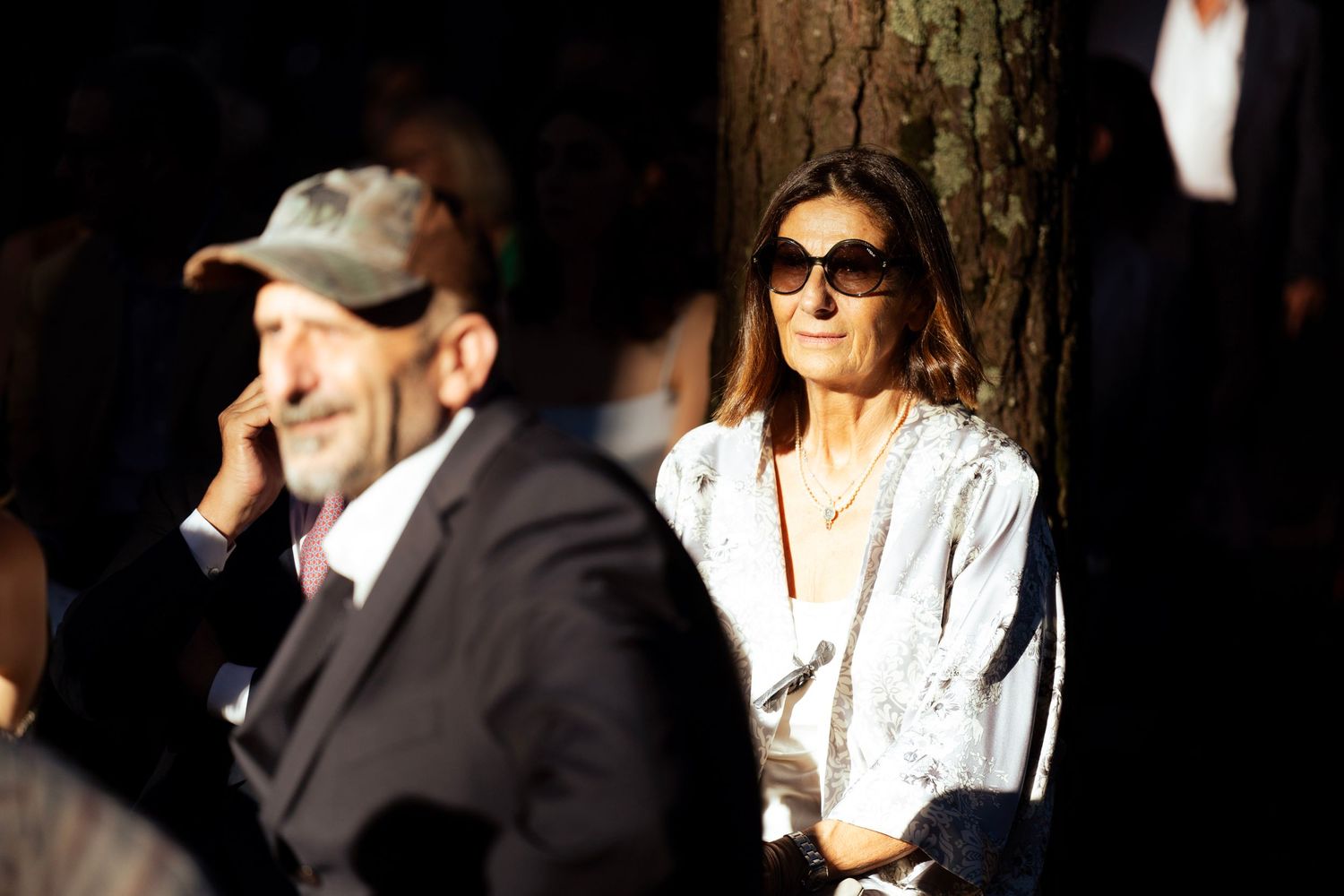 Wedding guests watch the ceremony while sitting among tall pine trees.