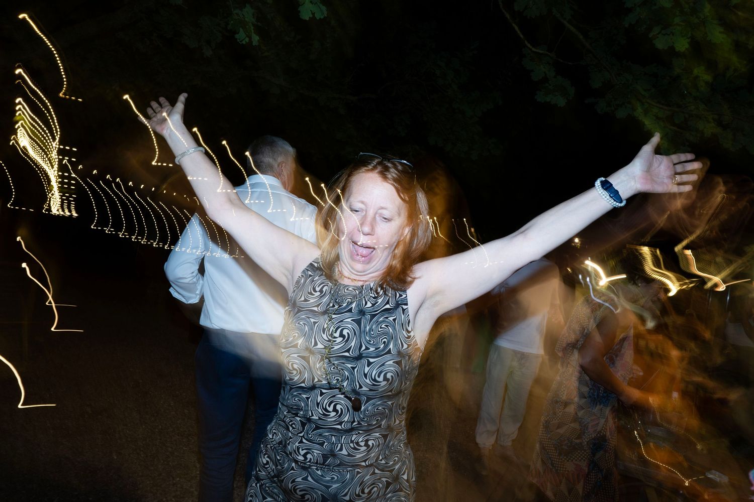 Celebratory dancer with arms raised under twinkling lights at night party.