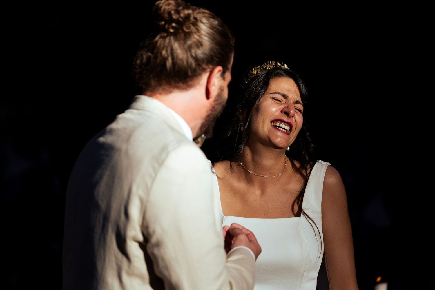 A candid moment between a couple laughing during a wedding ceremony in dim lighting.