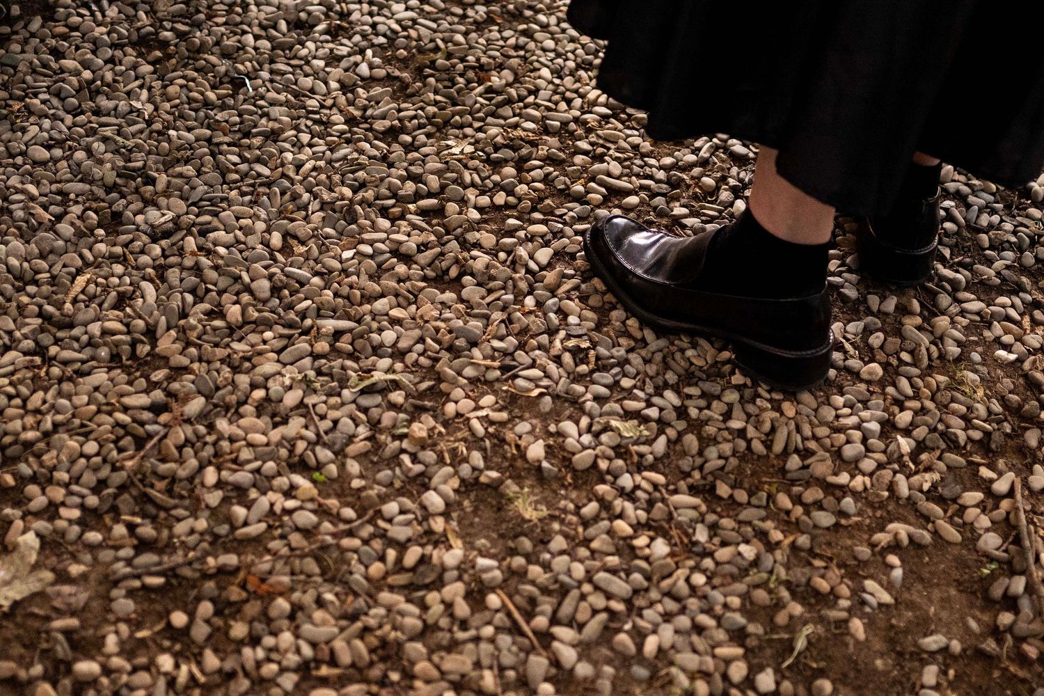 Black dress shoe standing on gravel or small stones ground texture.