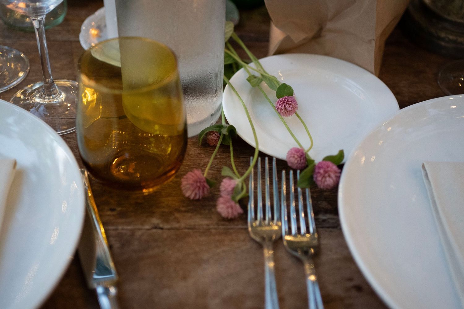 Table setting with pink flowers, wine glasses and silverware on rustic wooden surface.
