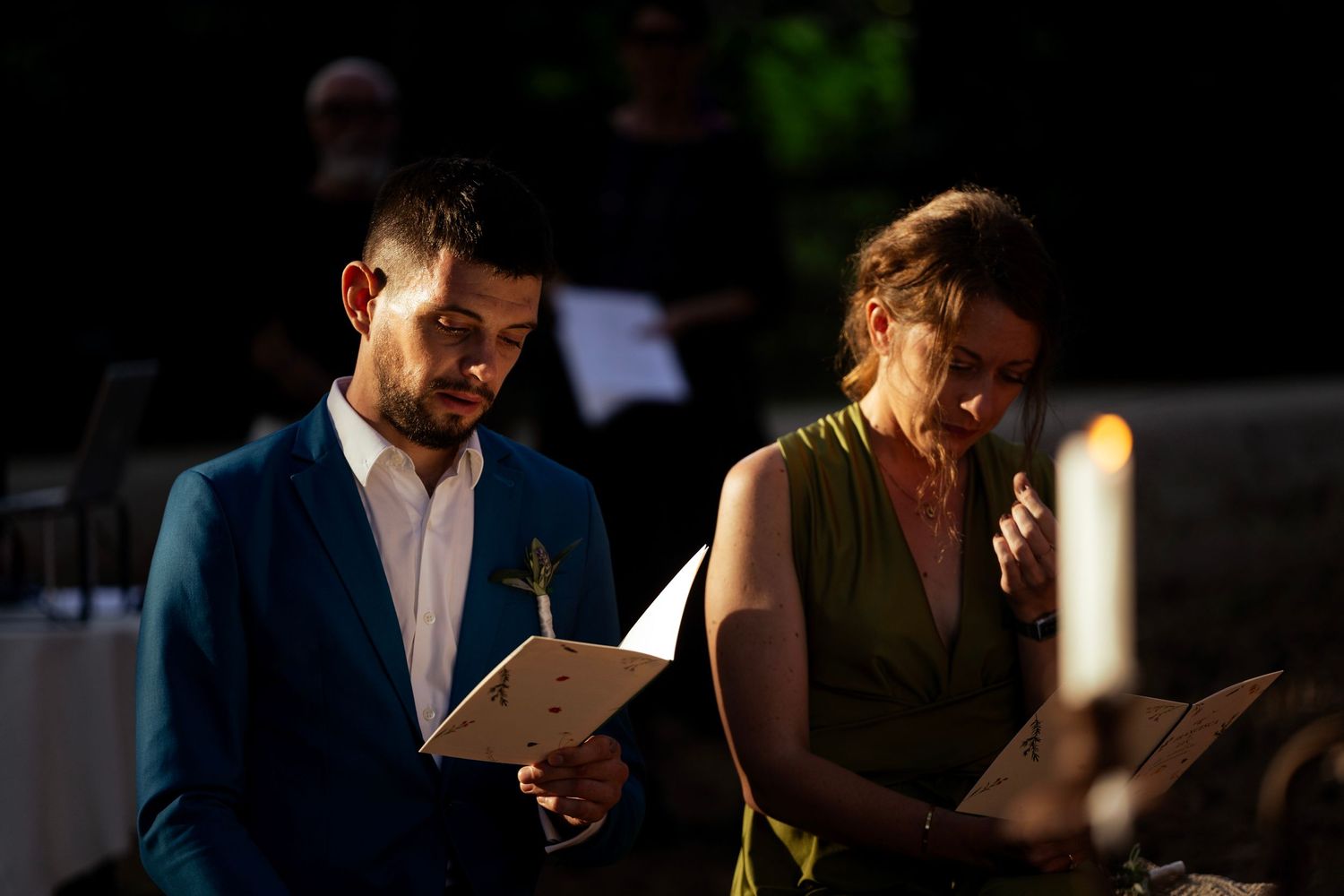 Wedding ceremony readings in a dimly lit forest setting with candles.