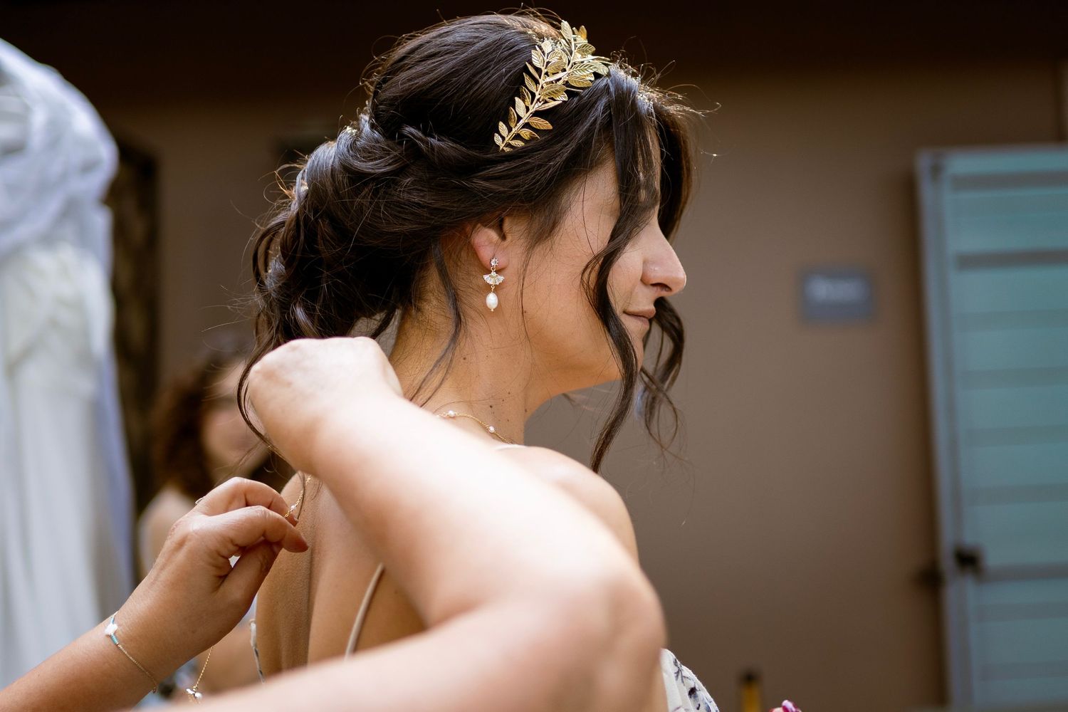 A person wearing a gold leaf crown has their dress adjusted from behind.