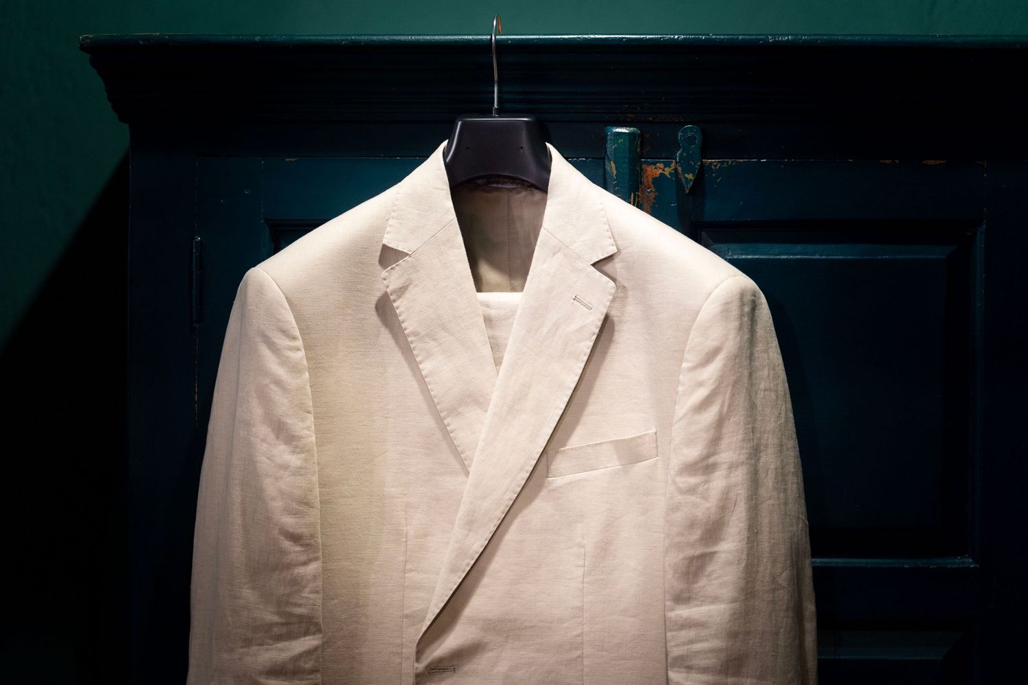 A cream colored suit jacket hanging on display against a dark background.