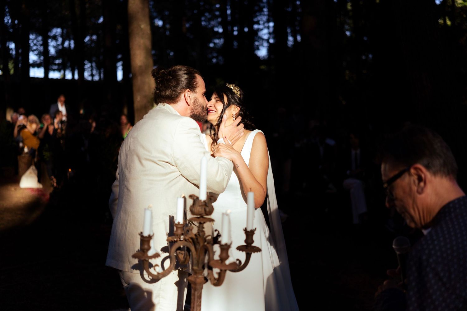 A couple embraces near a vintage candelabra during their evening forest wedding ceremony.