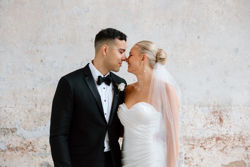 Close-up of wedding couple in formal attire against weathered wall backdrop.