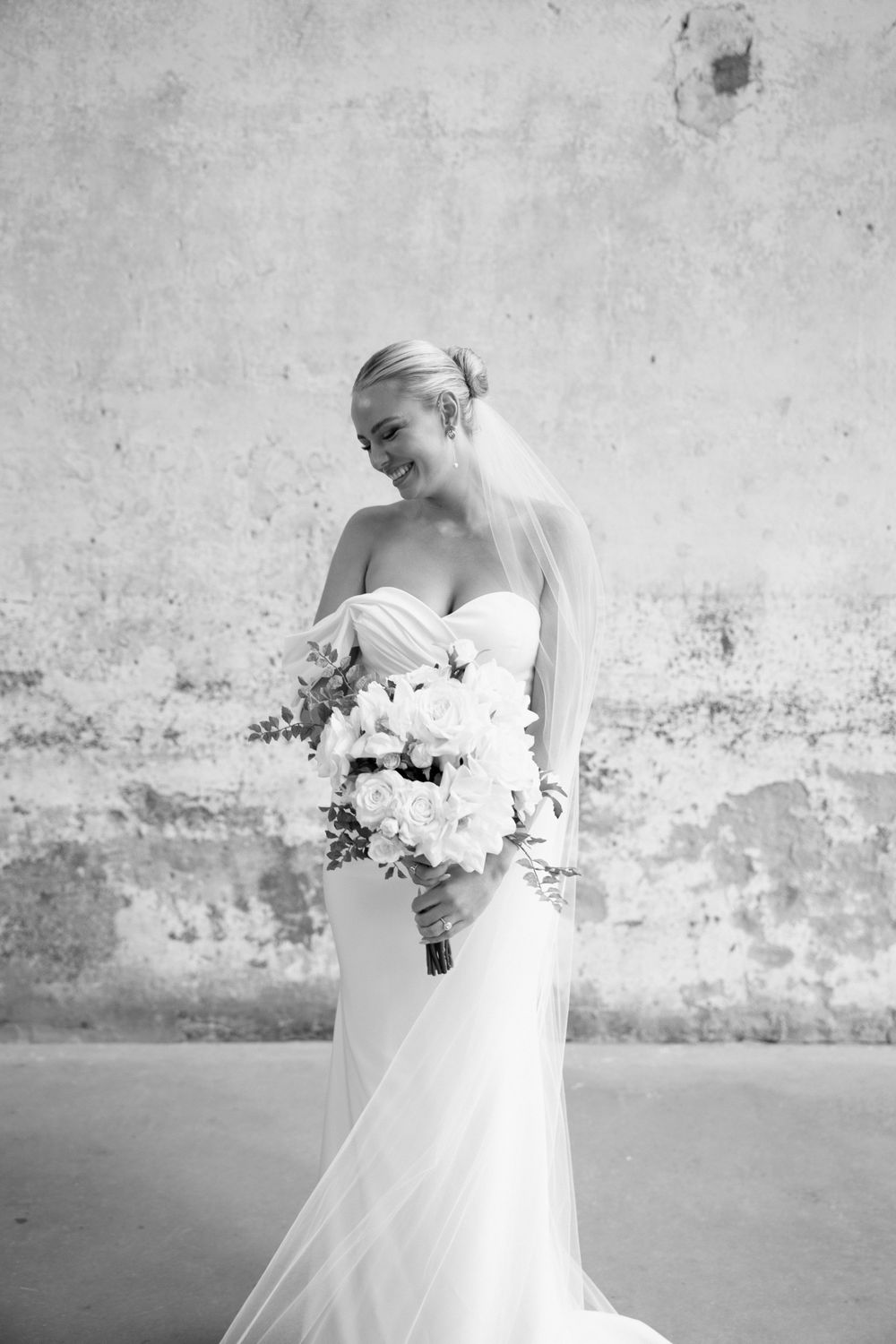 Black and white portrait of bride with white bouquet in classic wedding dress.