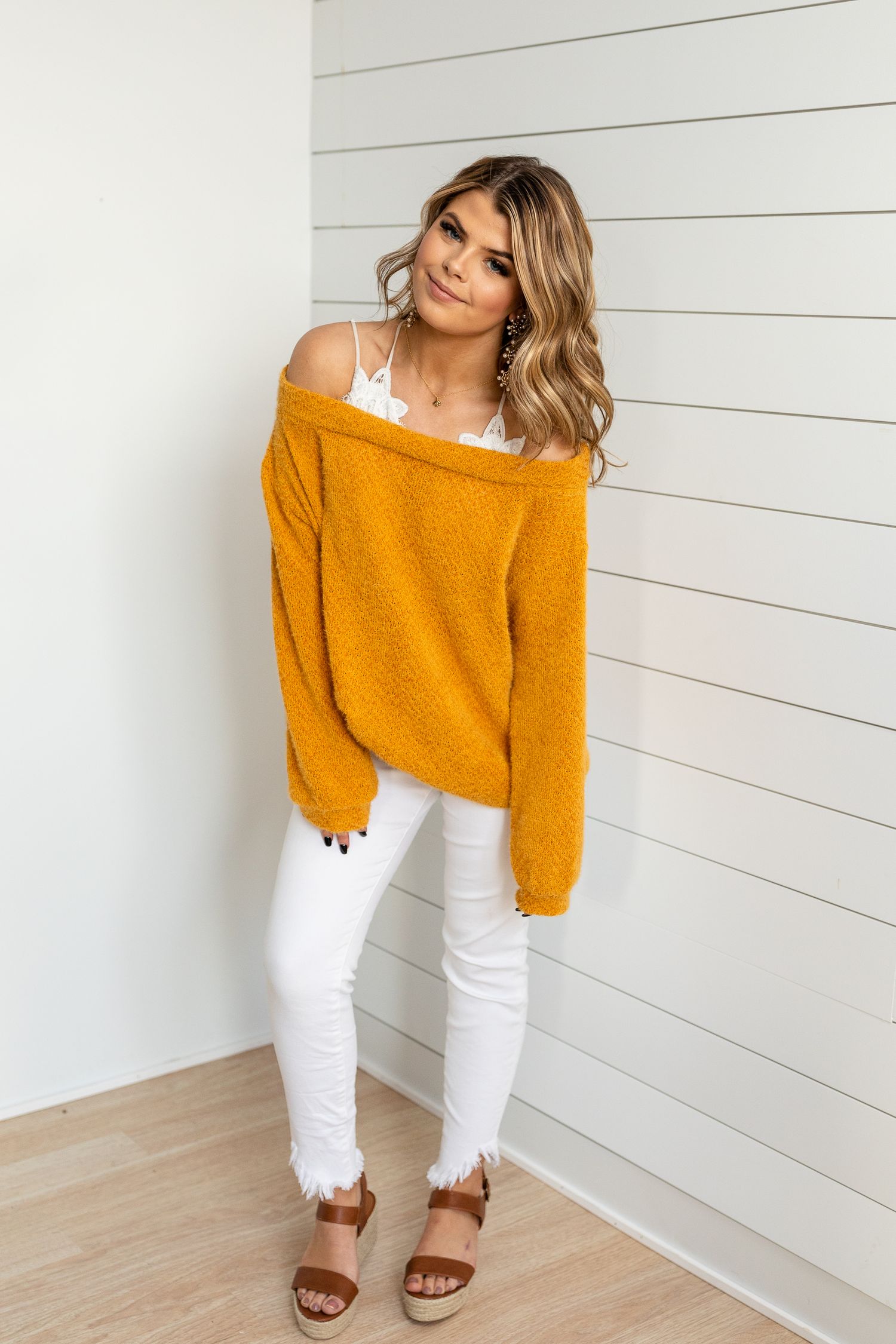 Woman in mustard sweater and white pants posing against shiplap wall.