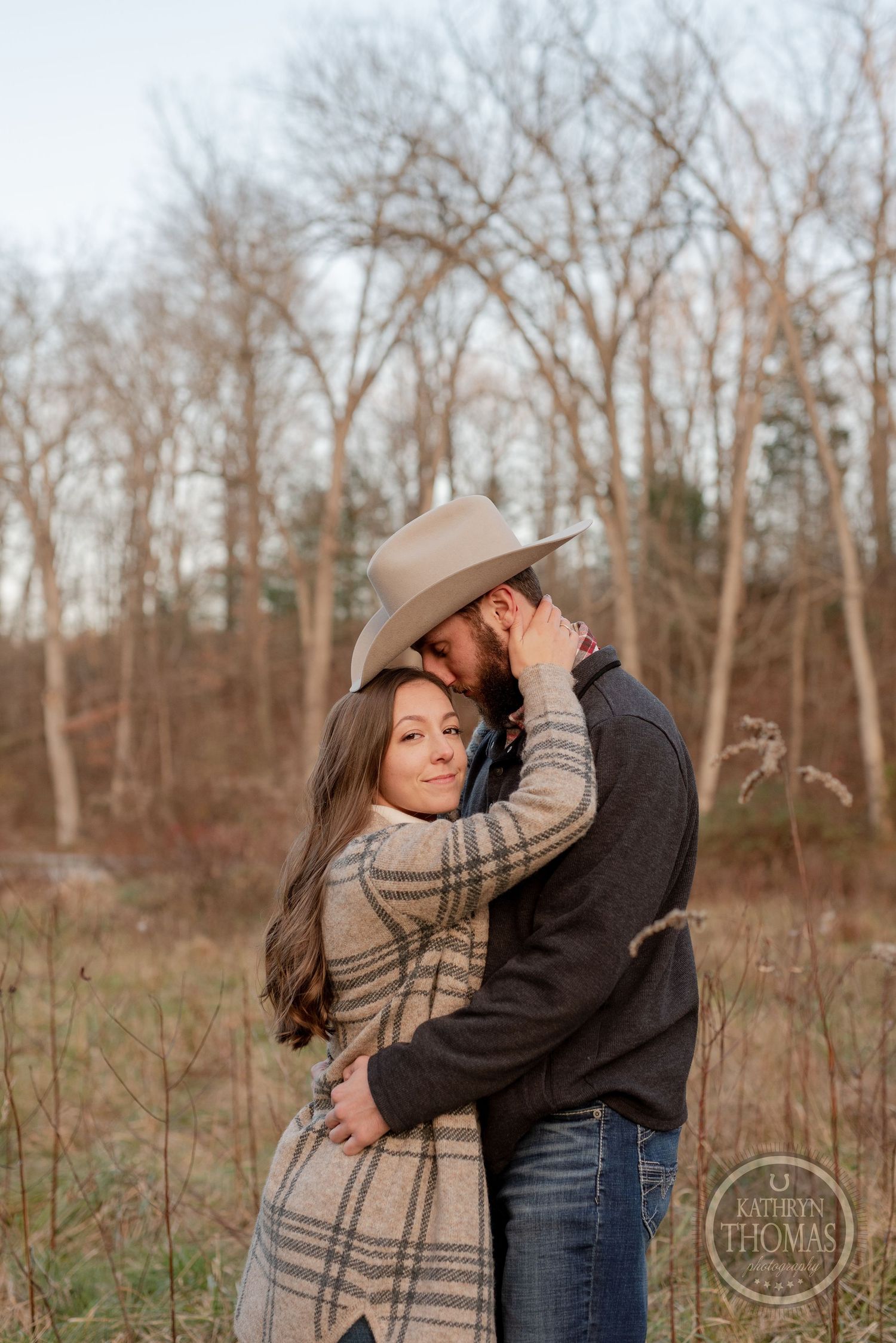 A tender moment shared between a couple wearing western attire in an autumn field.