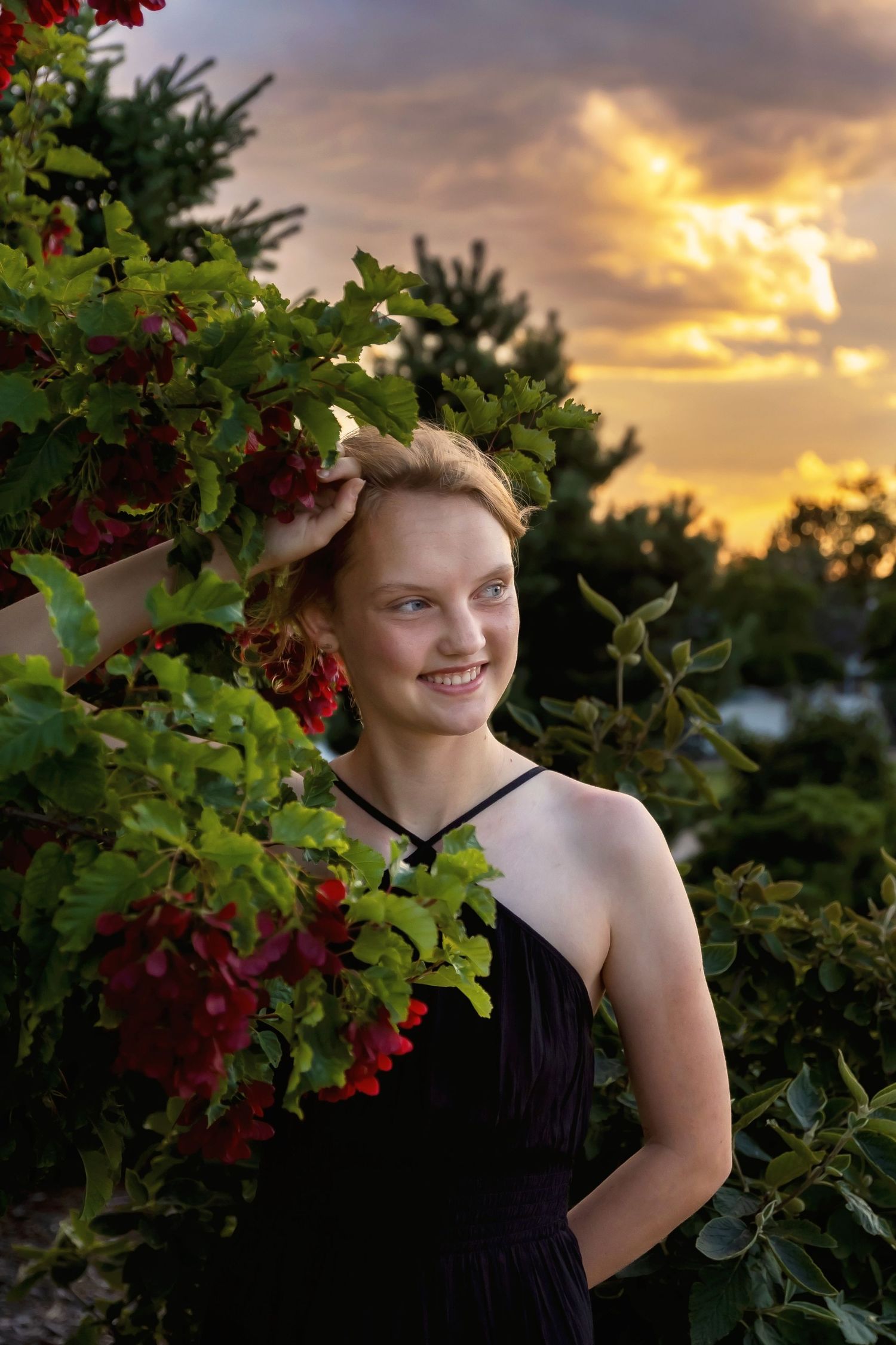 A portrait against a sunset sky with red berries and foliage in the foreground.