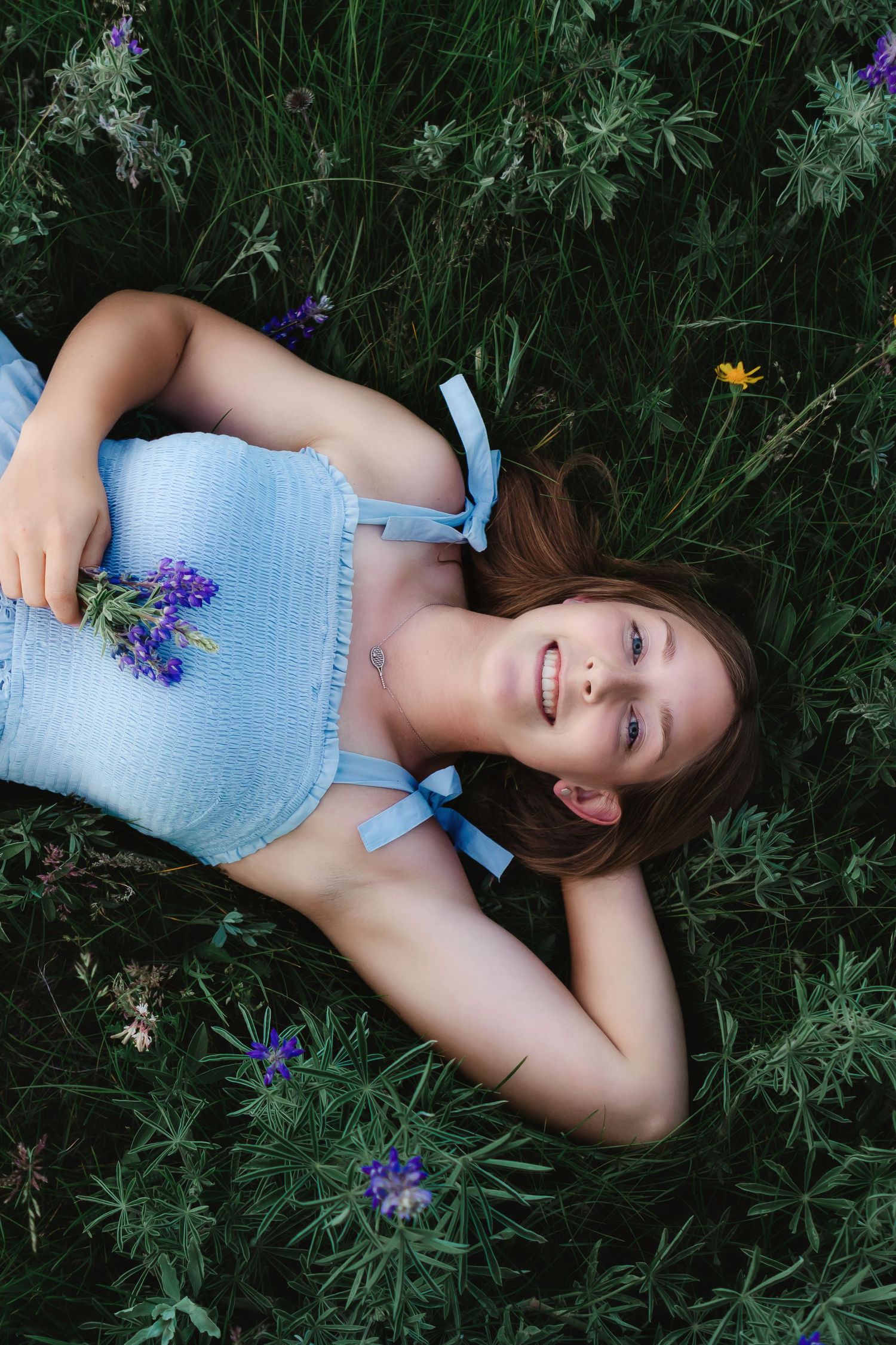 A joyful portrait of someone lying in wildflowers wearing a blue top with bow details.