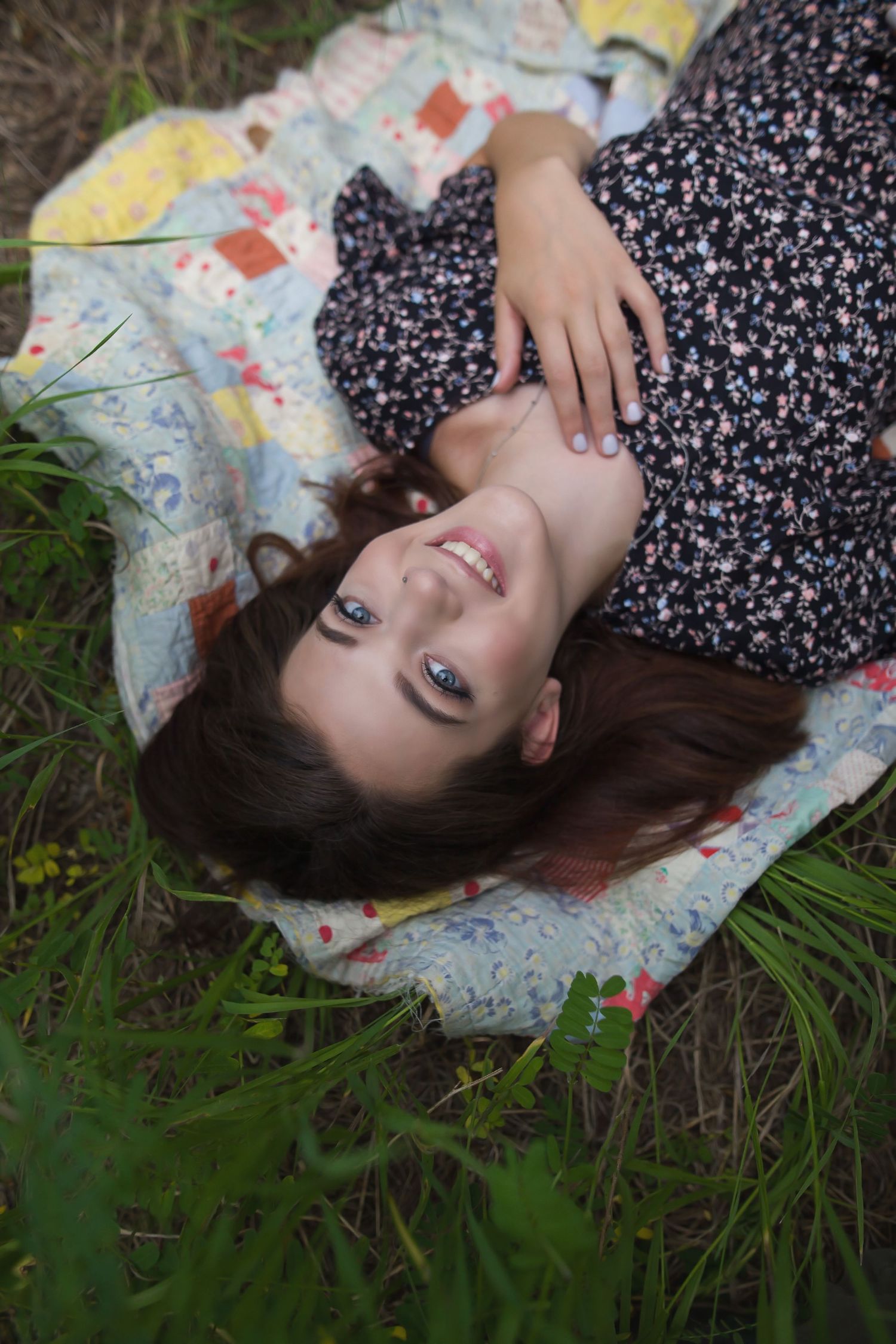 Artistic portrait lying on floral quilt in grass wearing floral dress.