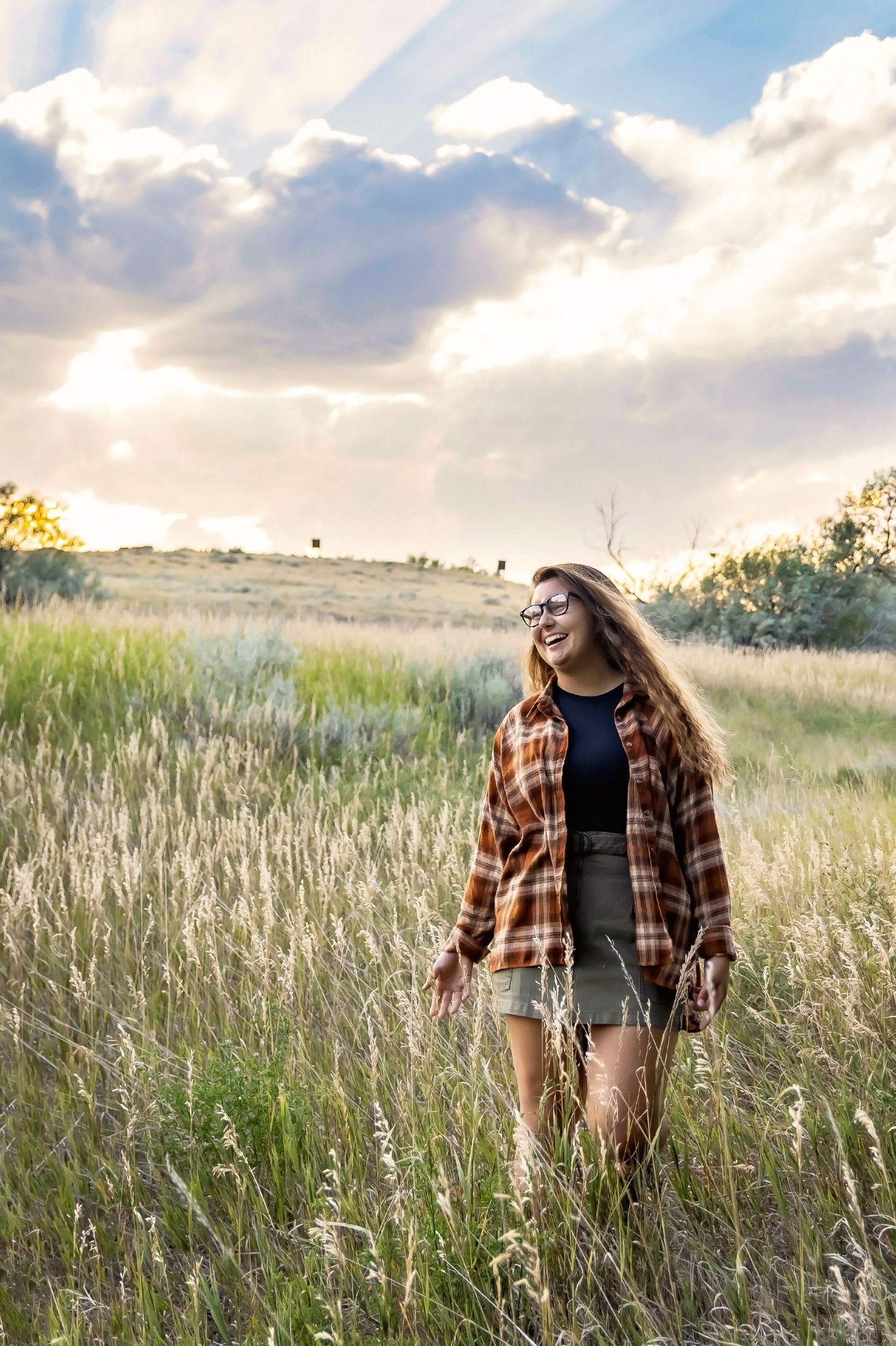 Person in plaid flannel and shorts walking through tall grass field at sunset.