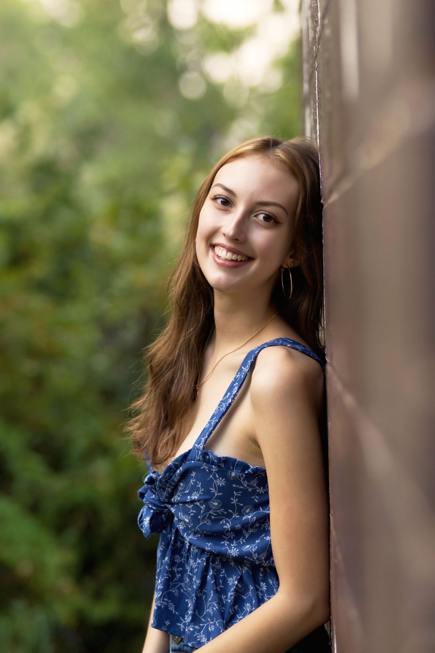Portrait of someone in blue dress leaning against wall with soft natural lighting.