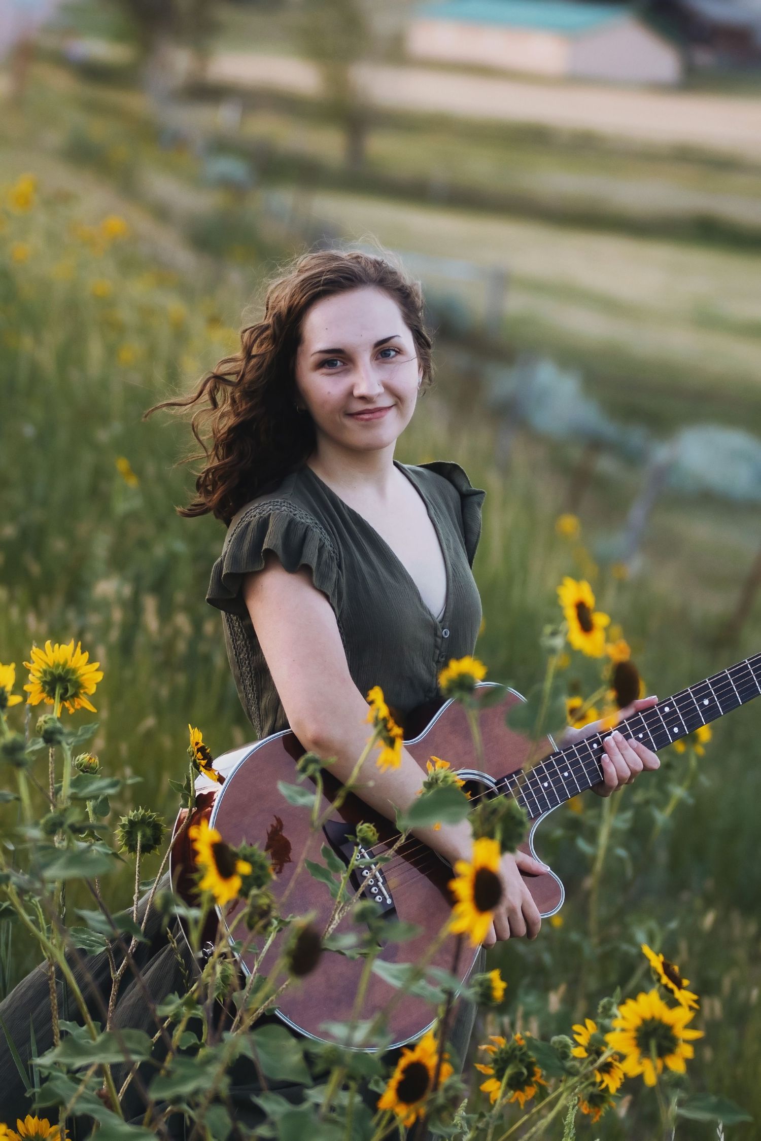 Musician with acoustic guitar posing in field of blooming sunflowers during golden hour.