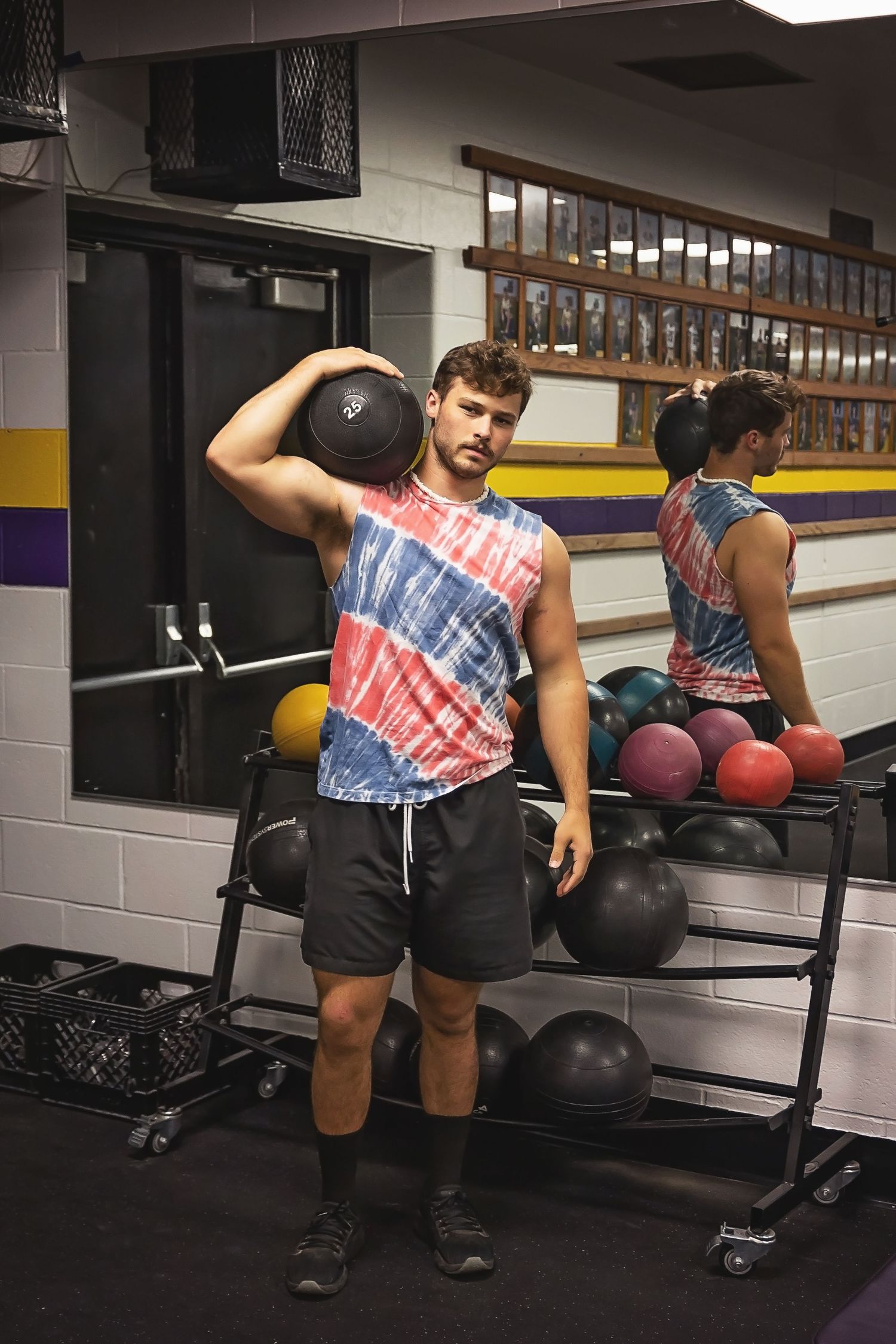 Athletic person in tie-dye shirt lifting medicine ball in gym setting.