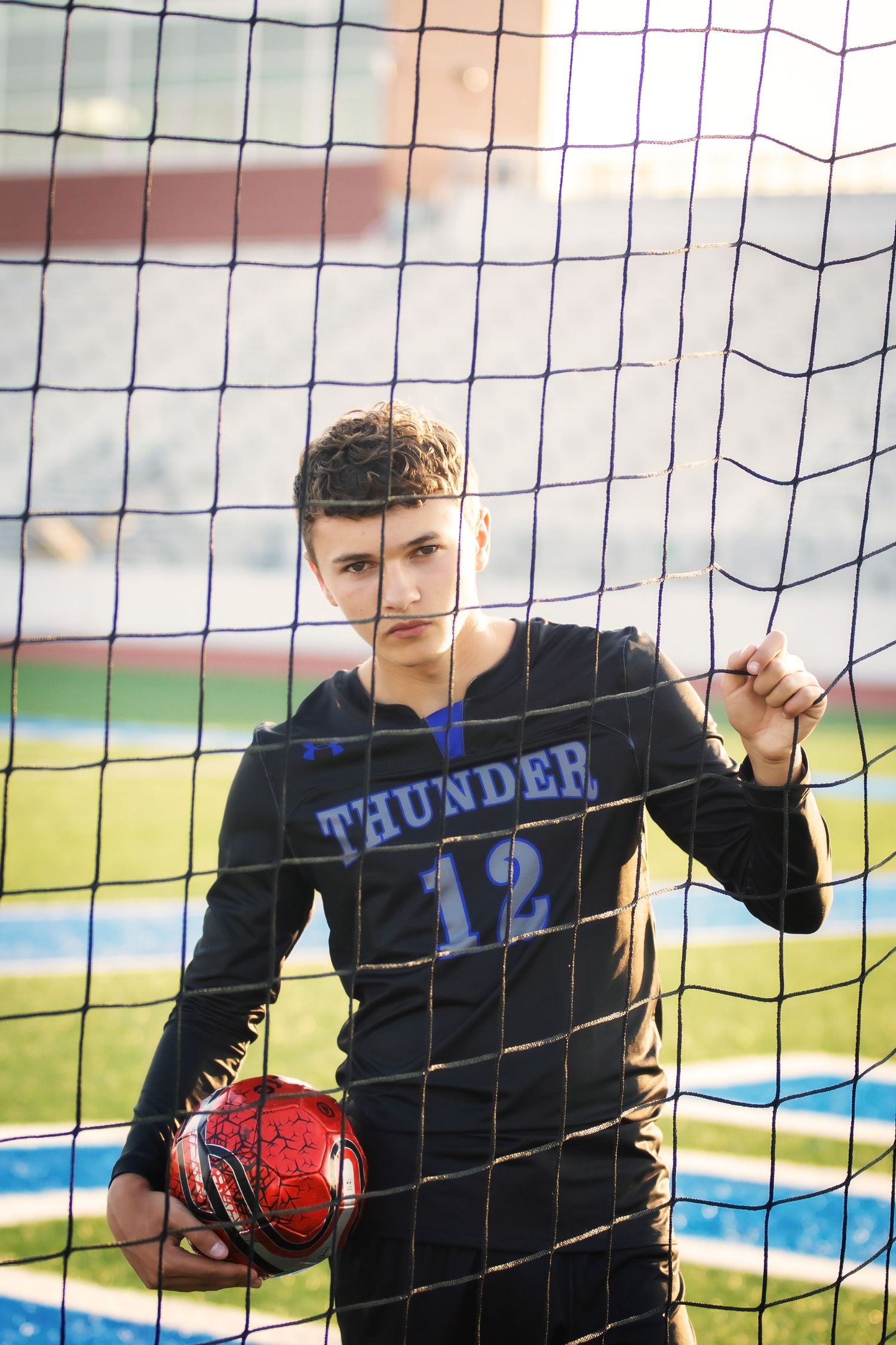 Soccer player in Thunder jersey number 12 poses with ball against goal net during sunset.