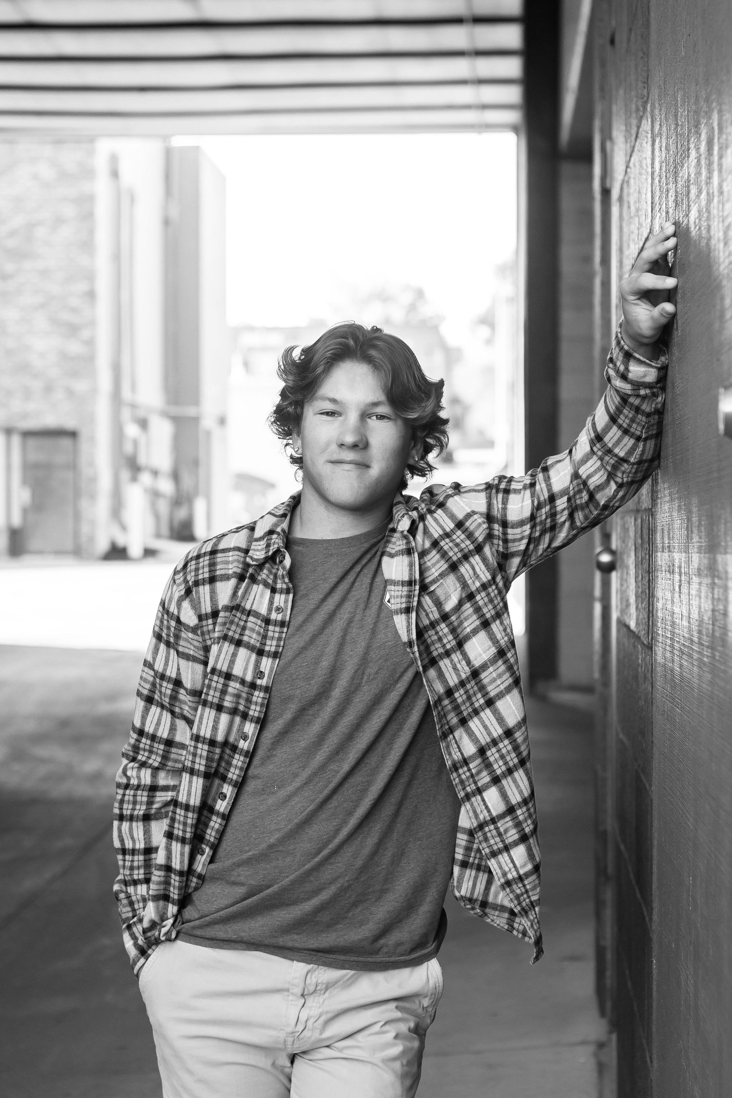 A casual portrait of someone leaning against a wall wearing a plaid shirt and jeans.