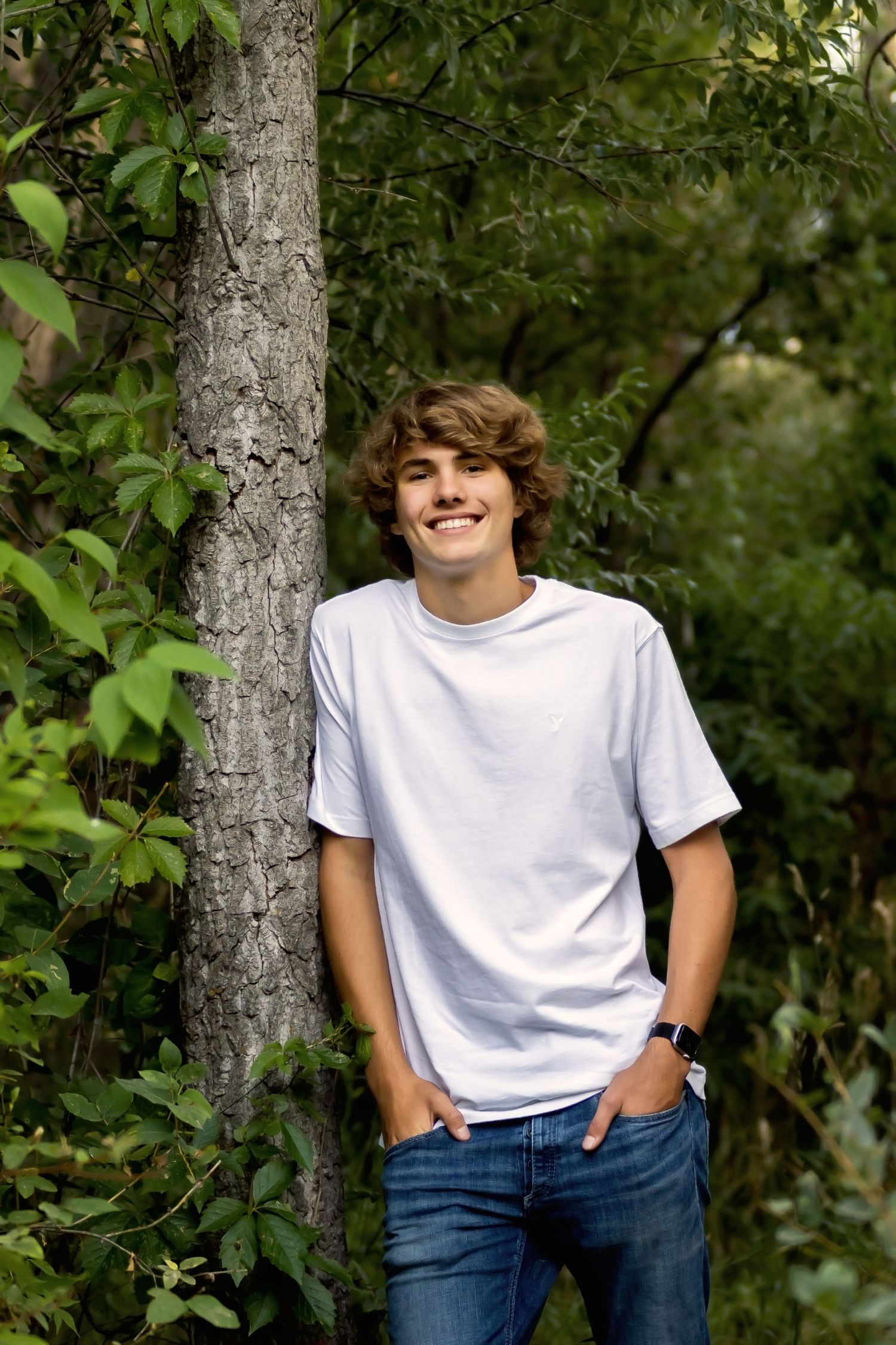 Casual outdoor portrait against tree trunk wearing white t-shirt and jeans.