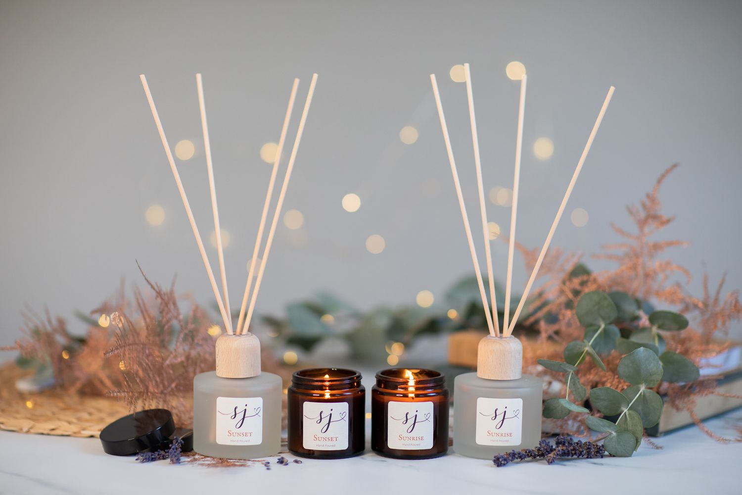 Cozy display of reed diffusers, candles and eucalyptus on gray background with soft lighting.
