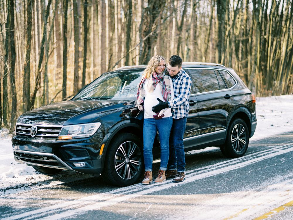 Couple standing next to black SUV on snowy winter road.