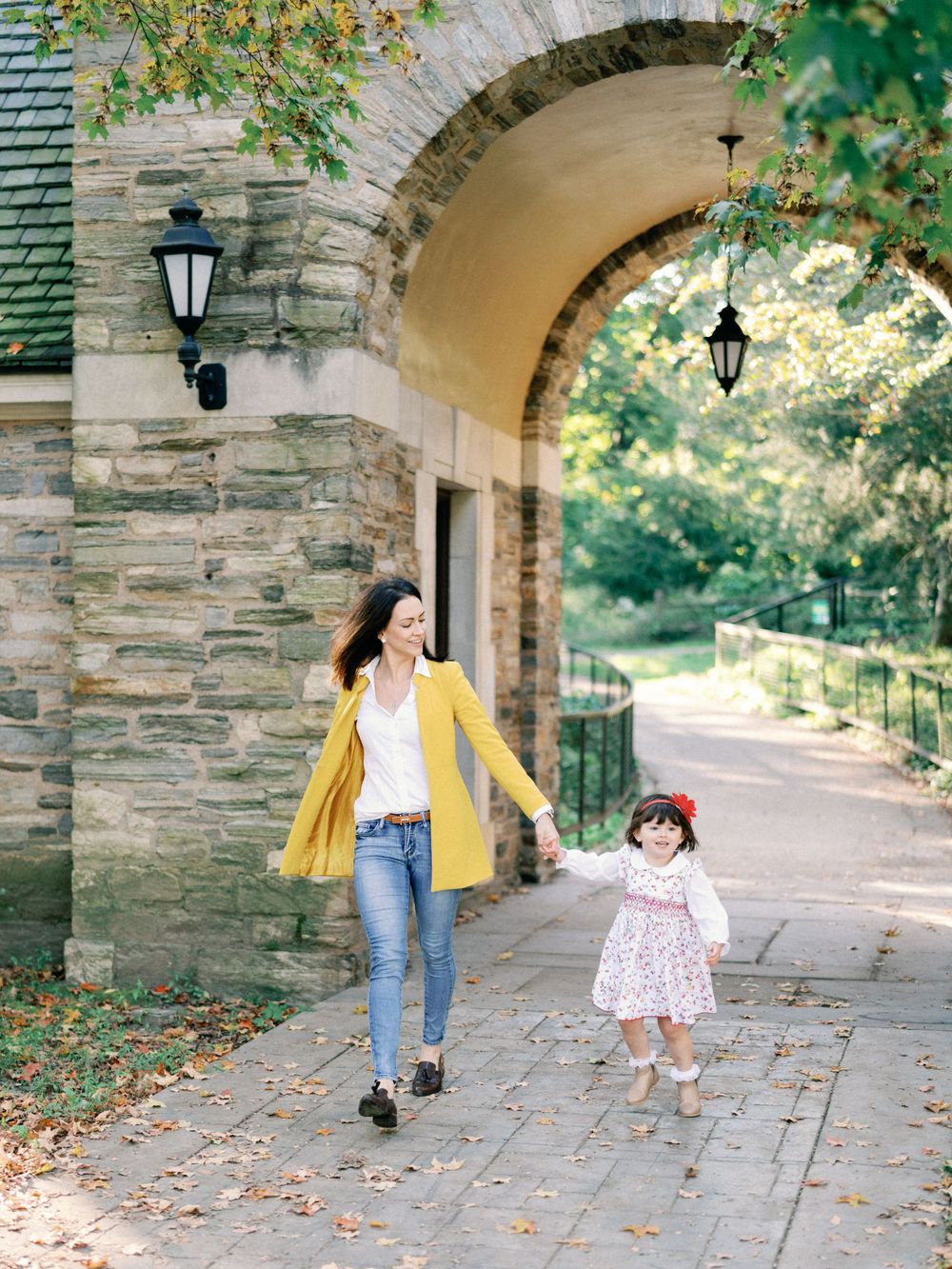 Casual stroll under architectural stone archway with autumn leaves scattered.