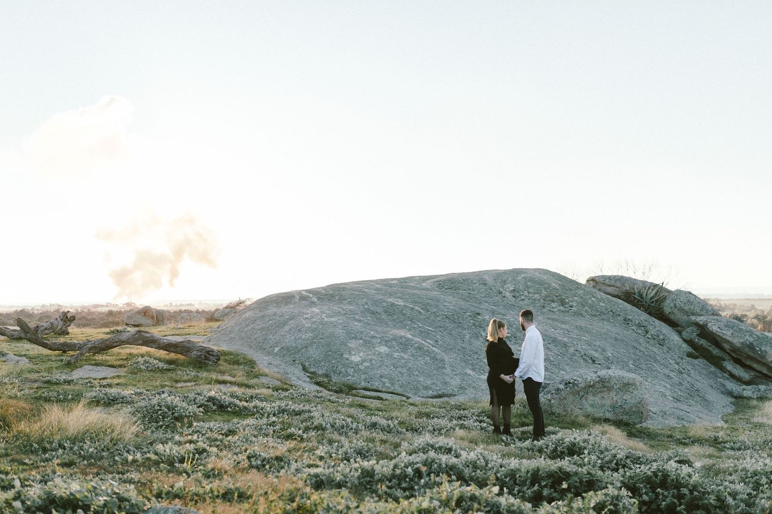 Two figures standing together on a rocky hilltop against a bright sky.
